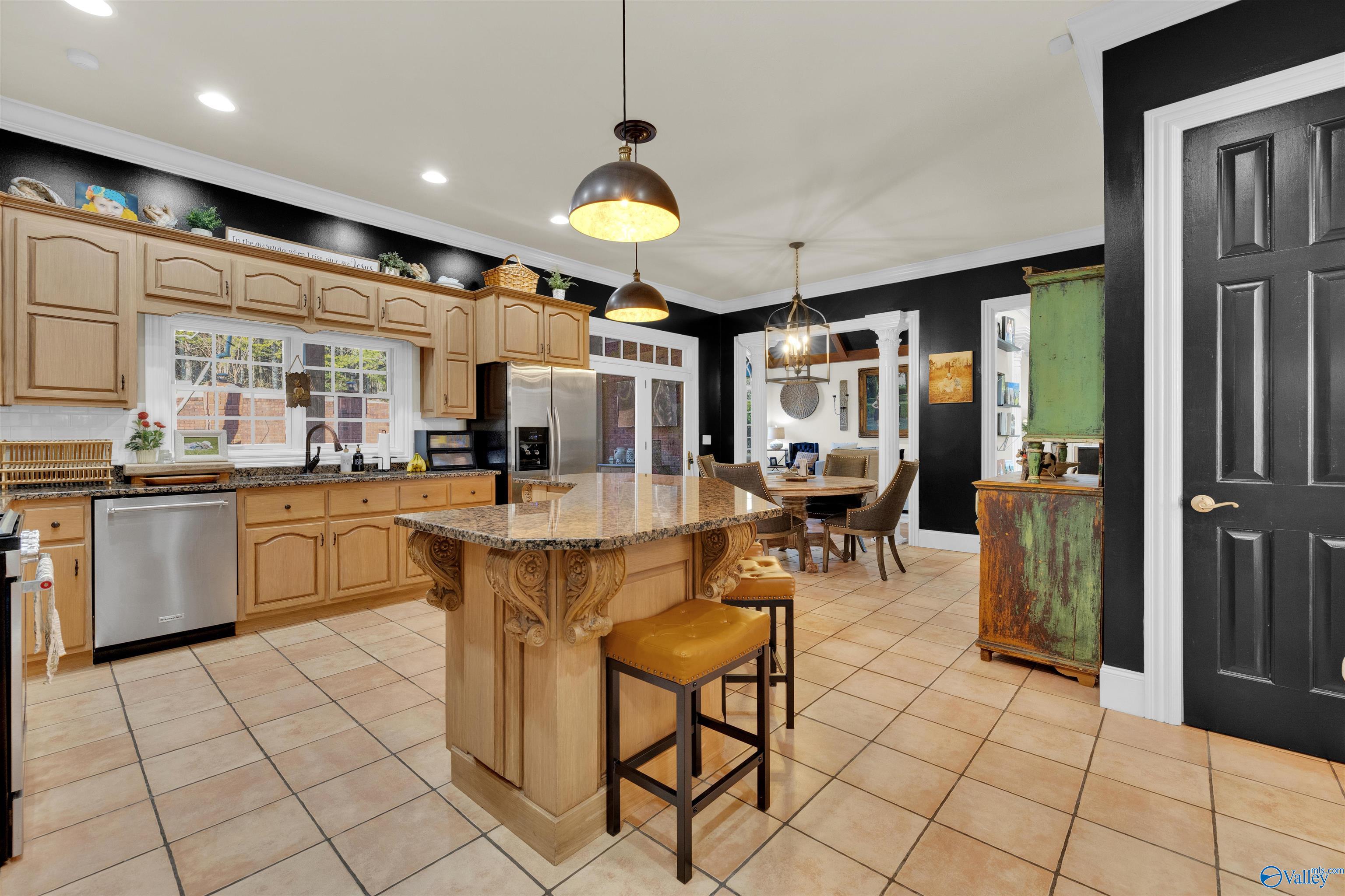 Kitchen with light wood cabinetry, black walls, and a granite island with carved supports.