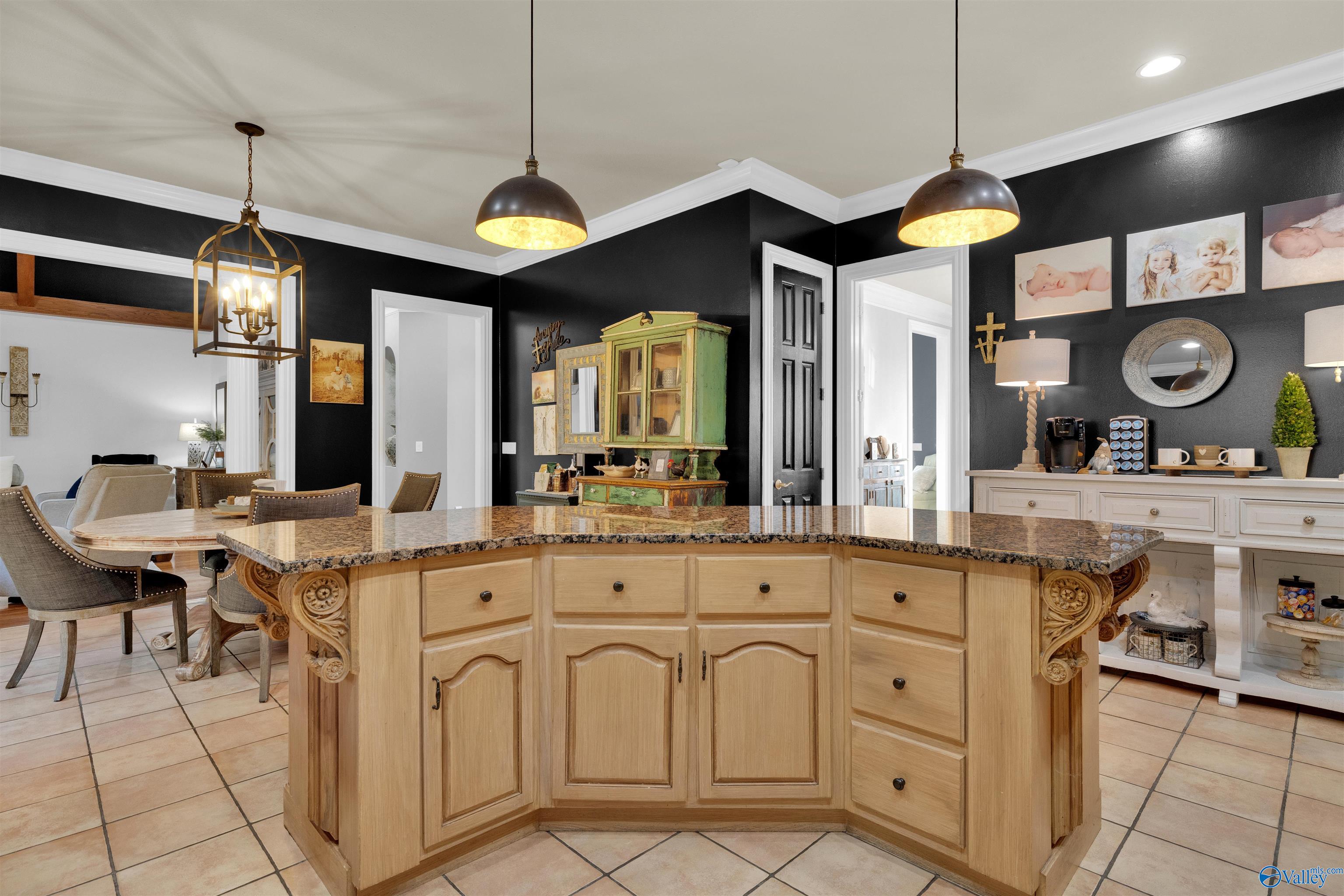 Kitchen with a carved wood island, granite countertop, black walls, and built-in coffee bar.