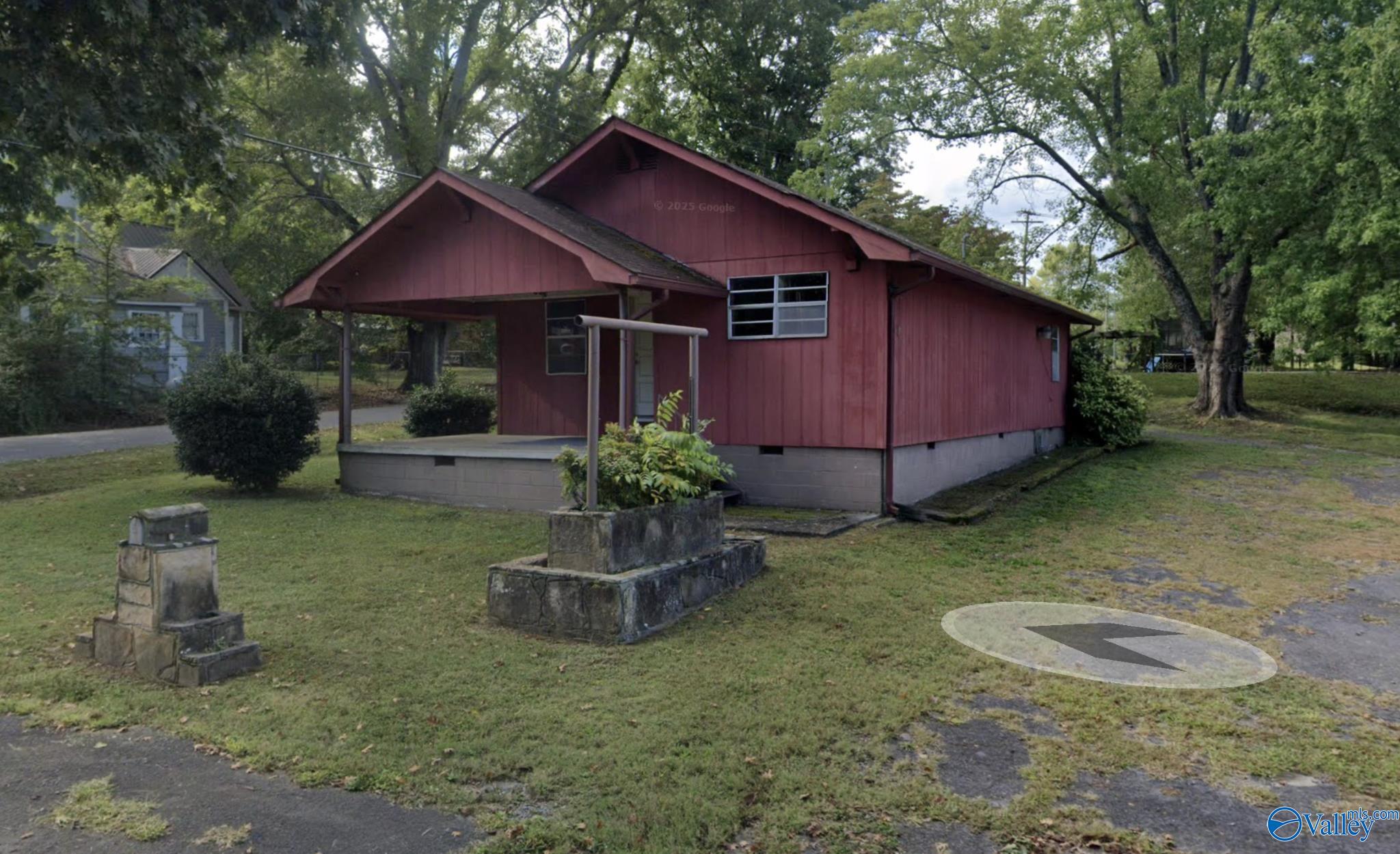 Red-sided house with a covered porch on a grassy, tree-shaded lot.