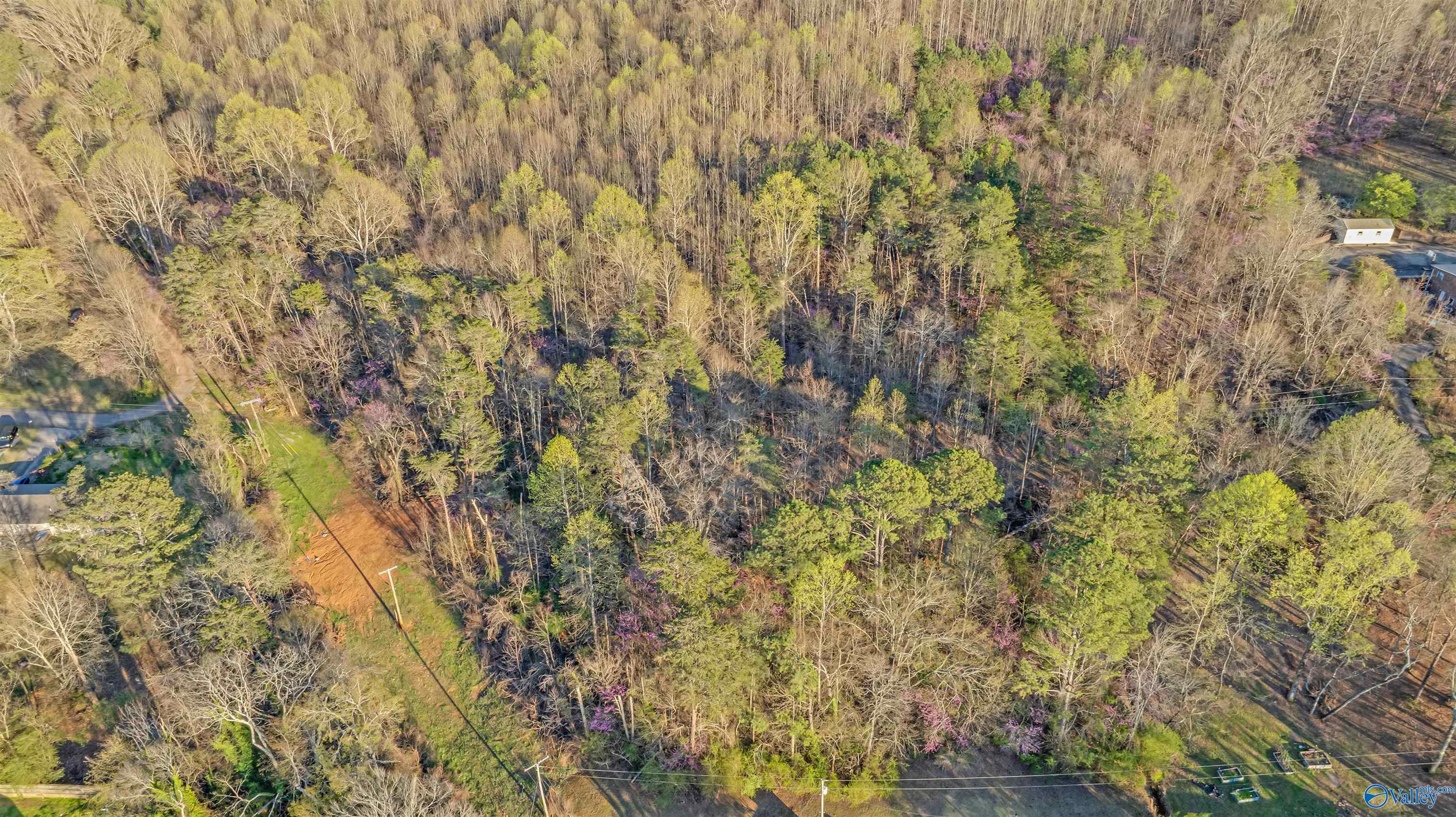Aerial view of a wooded lot with a cleared strip and nearby utility lines.