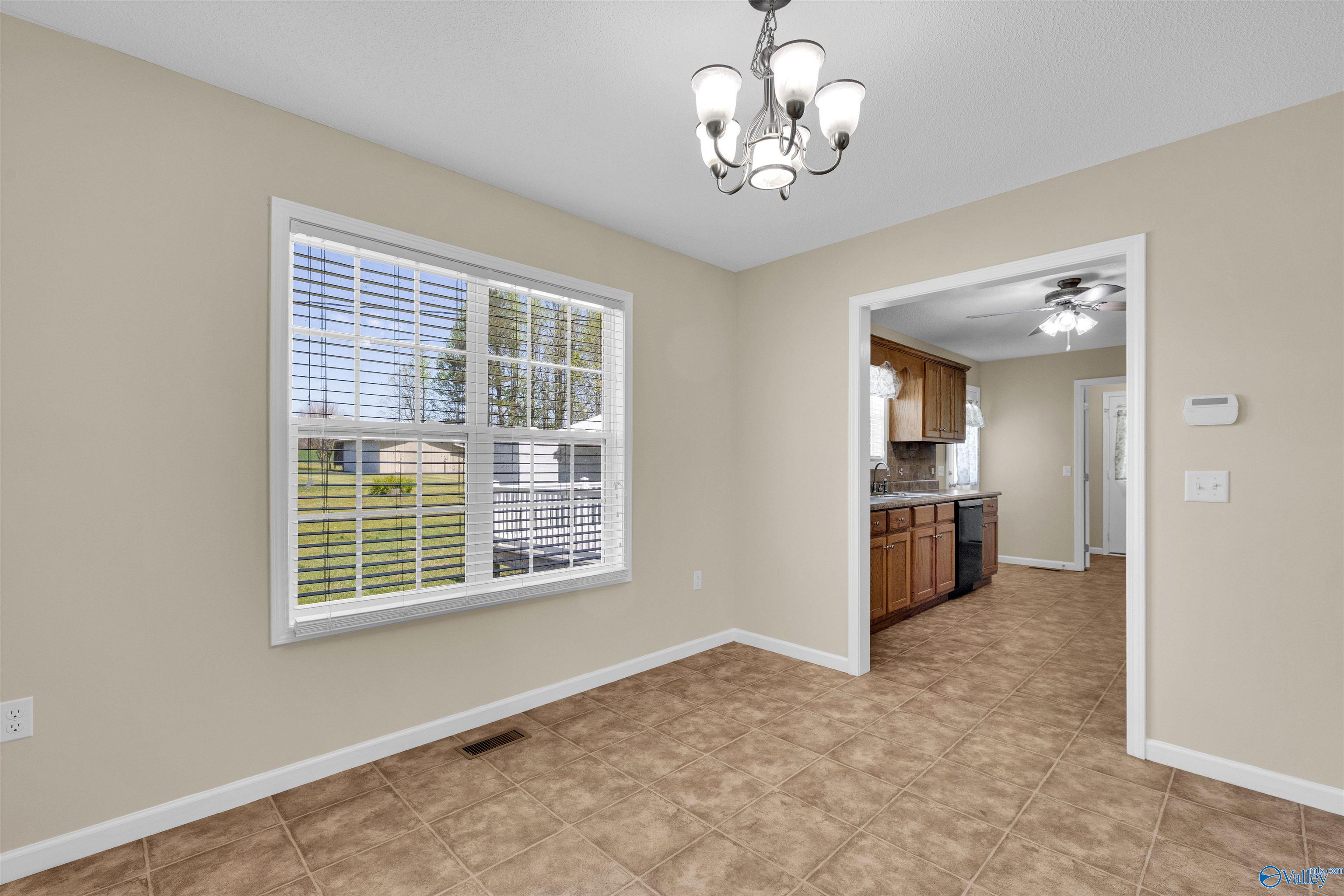 Empty dining room with brown tile floors, a chandelier, and a large window overlooking the yard.