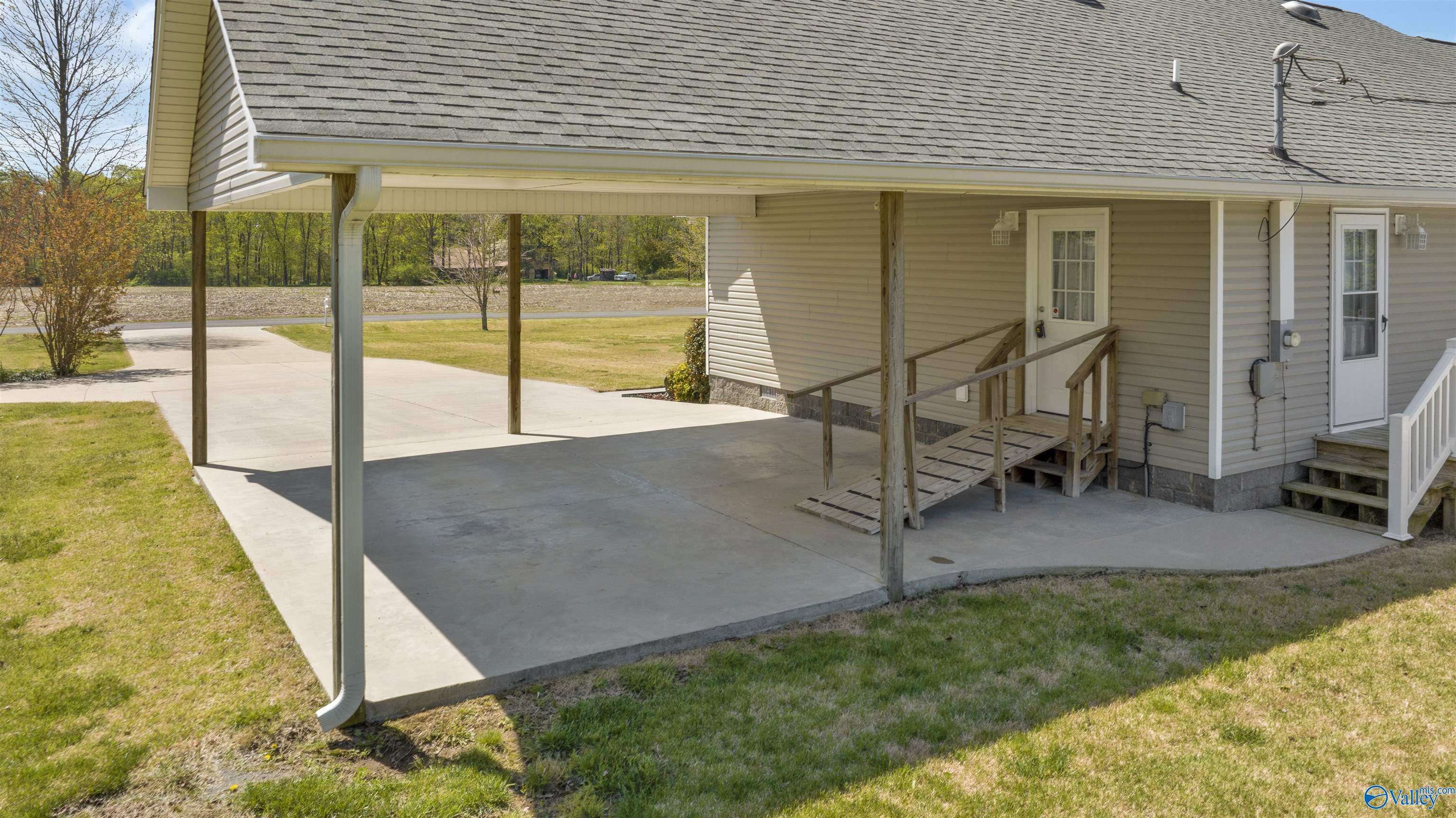House exterior with a covered concrete carport and wooden accessibility ramp beside the lawn.