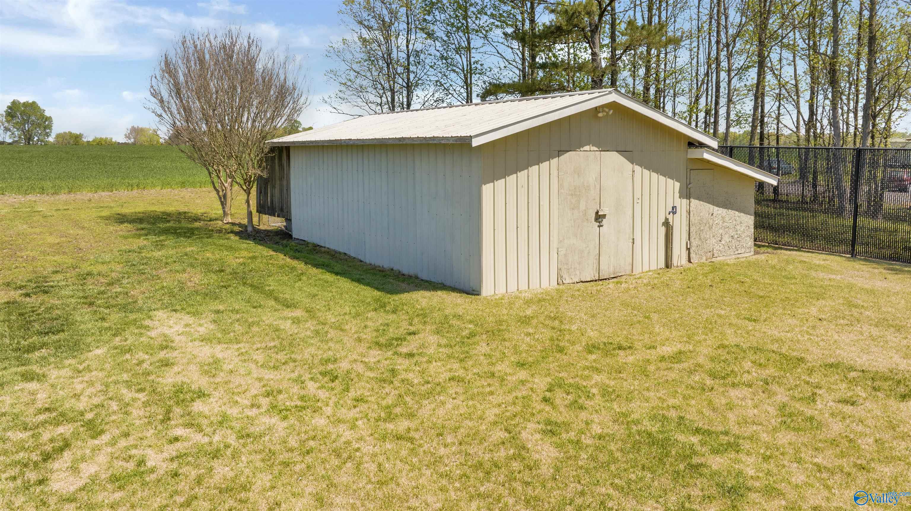 Beige metal outbuilding with a white gabled roof beside a black metal fence.