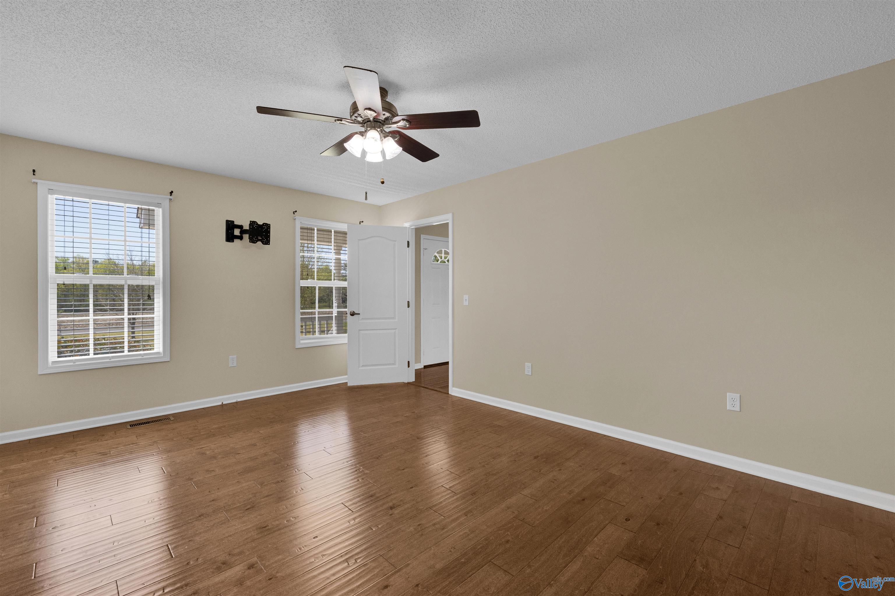 Empty room with hardwood floors, two windows, and a ceiling fan with lights.