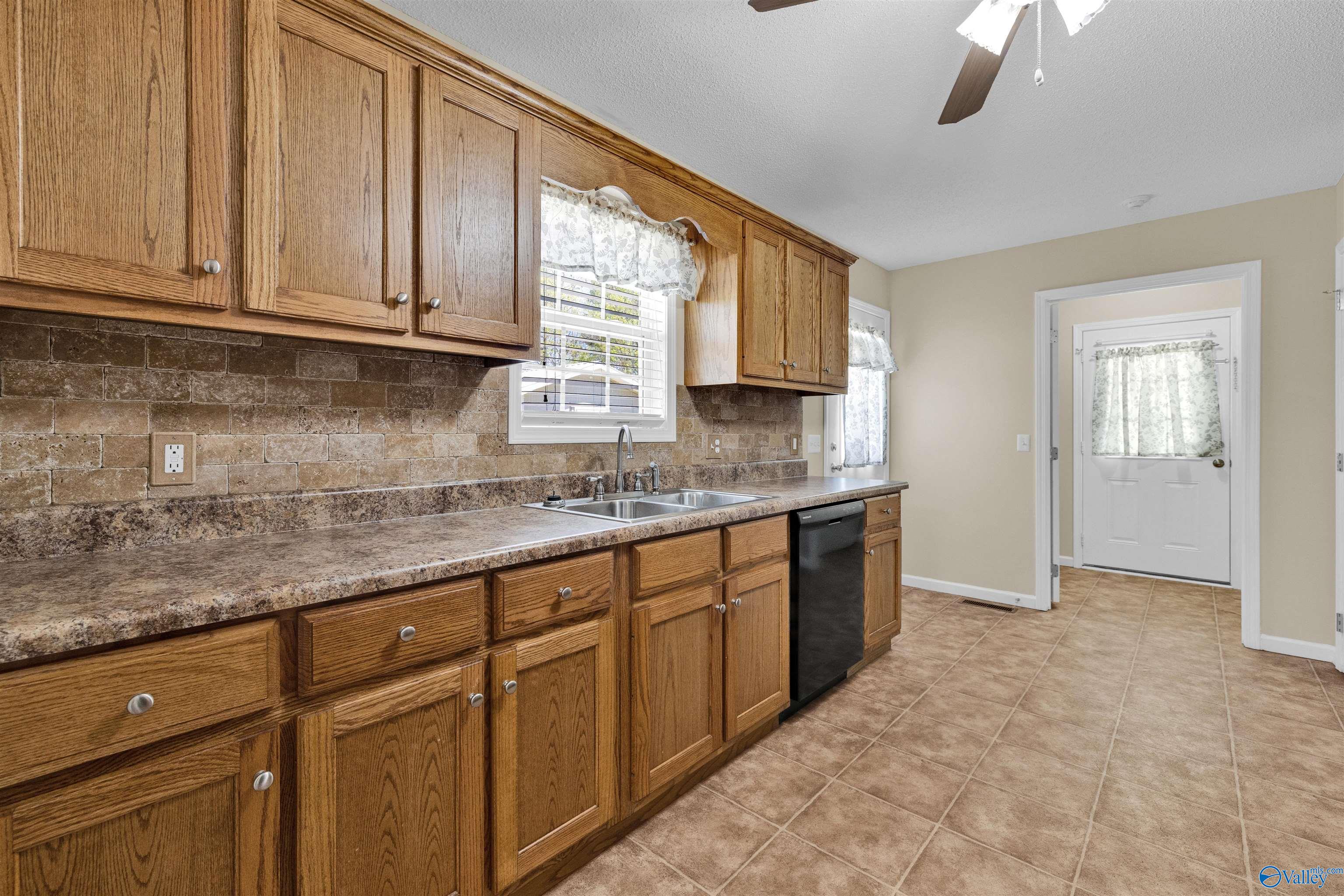Kitchen with oak cabinetry, tiled backsplash, double sink, and black dishwasher.
