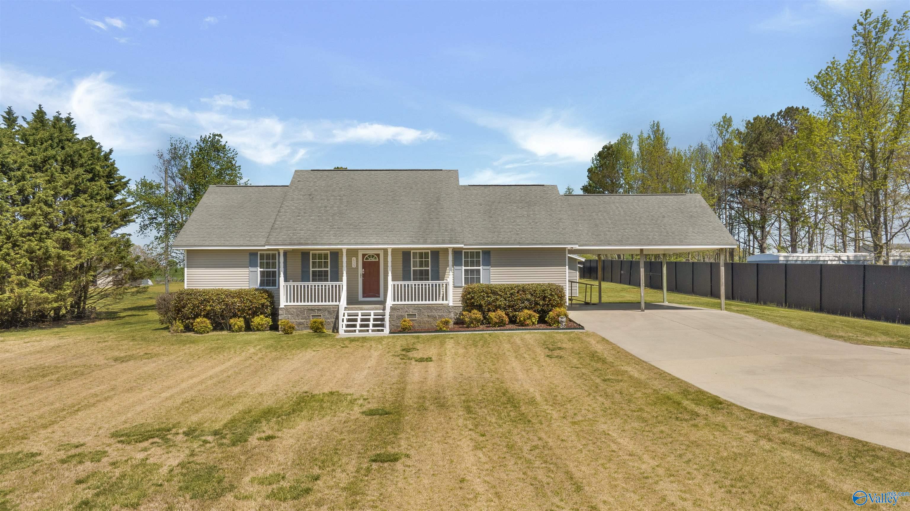 Single-story gray home with a white porch, red door, and attached carport beside a wide driveway.