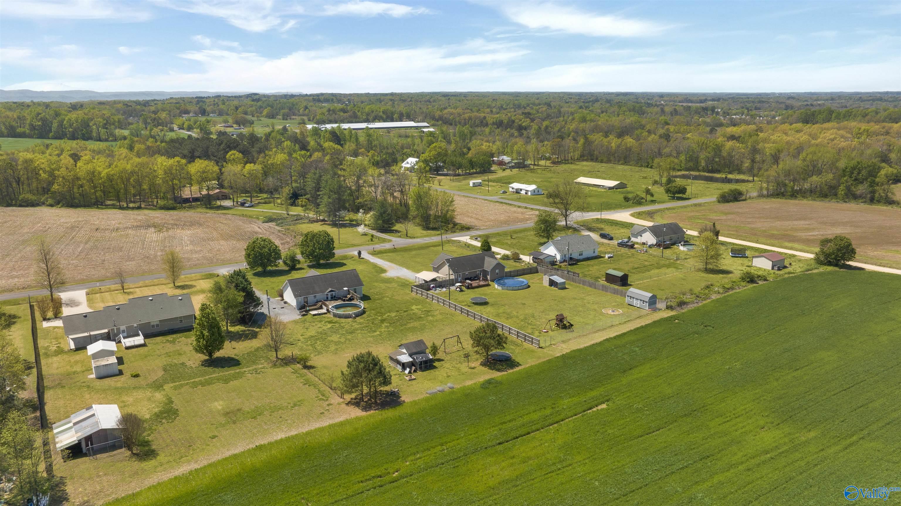 Aerial view of rural homes and fenced yards beside a broad green field.