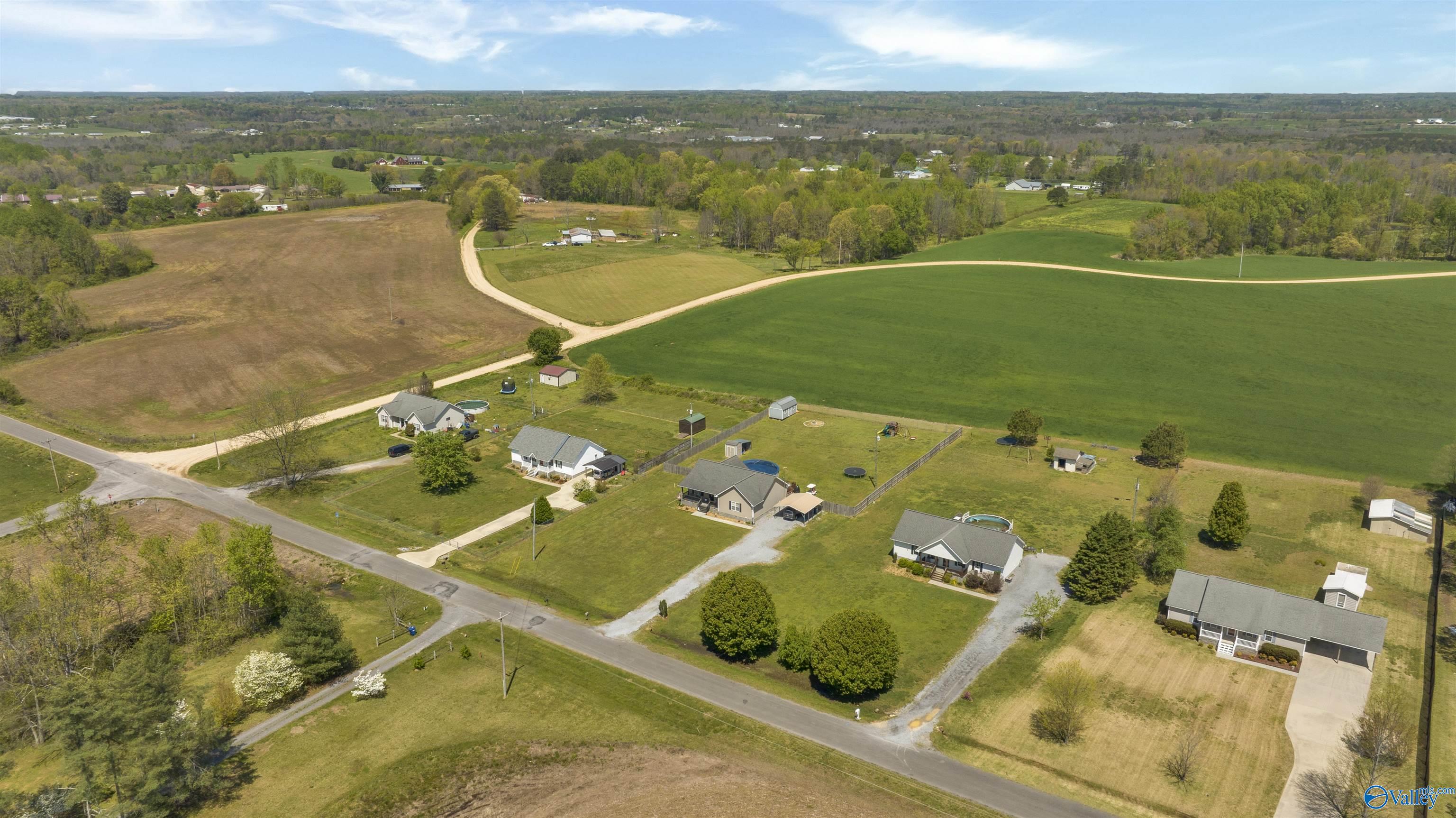 Aerial view of rural homes beside open fields, with lawns, trees, and winding gravel roads.