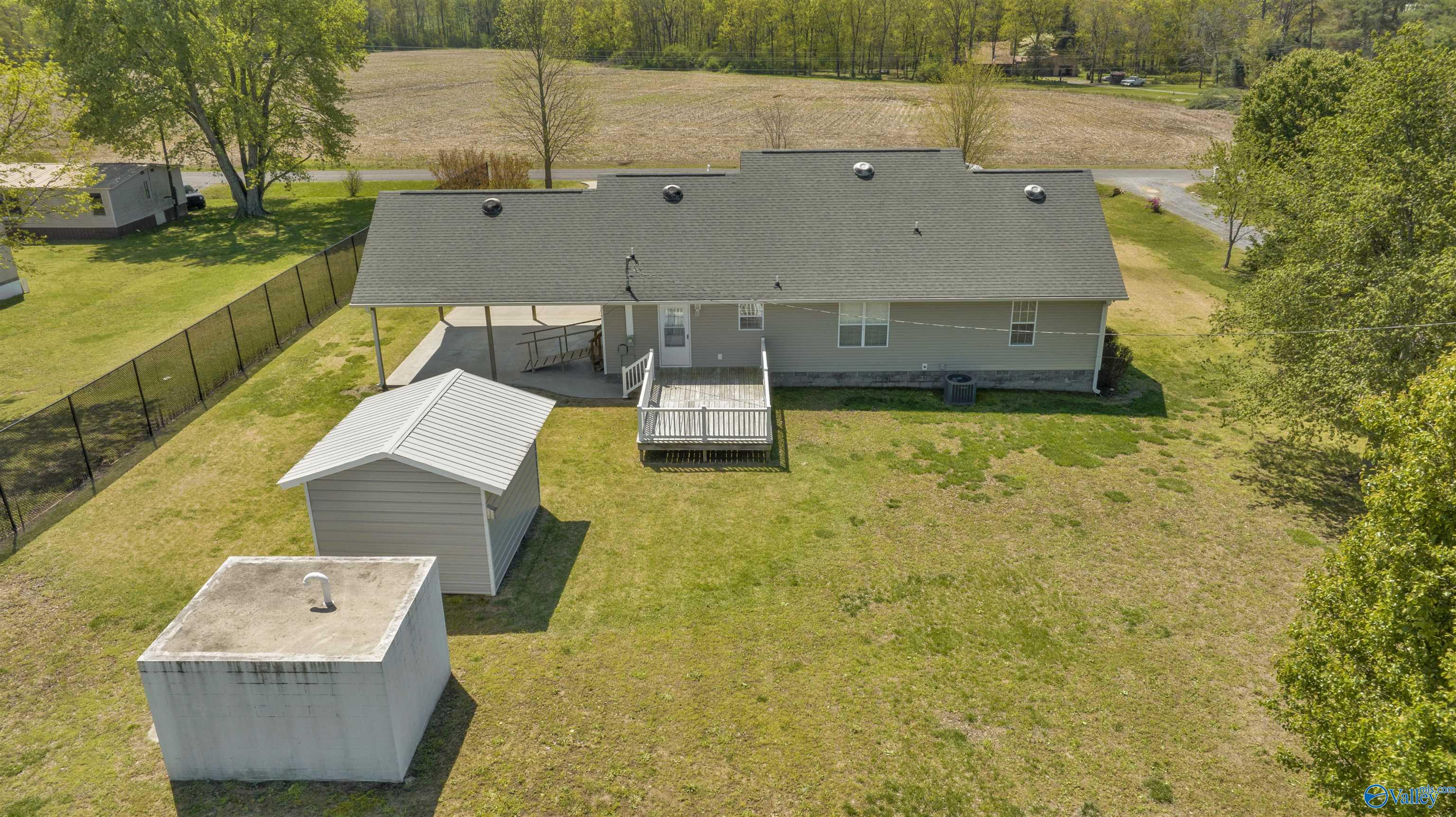 Aerial rear view of a gray house with a covered patio, deck, detached shed, and spacious yard.
