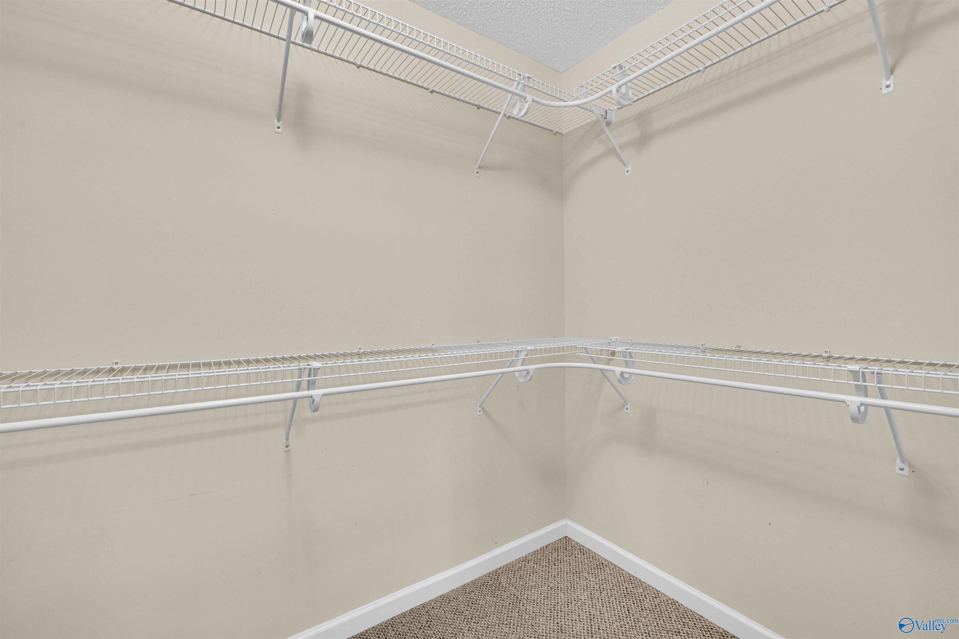 Empty walk-in closet with white wire shelving and hanging rods.