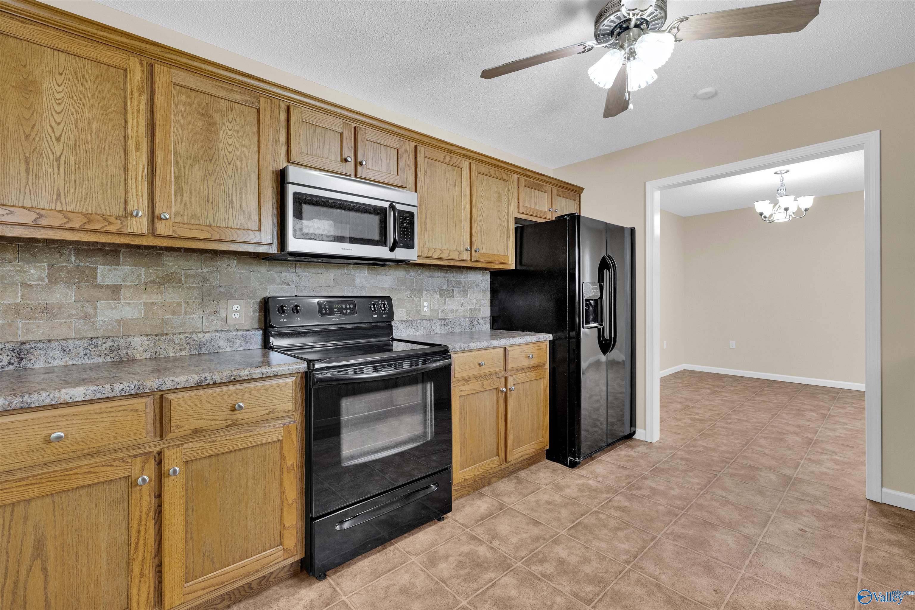 Kitchen with oak cabinets and black appliances, opening into an empty tiled room.