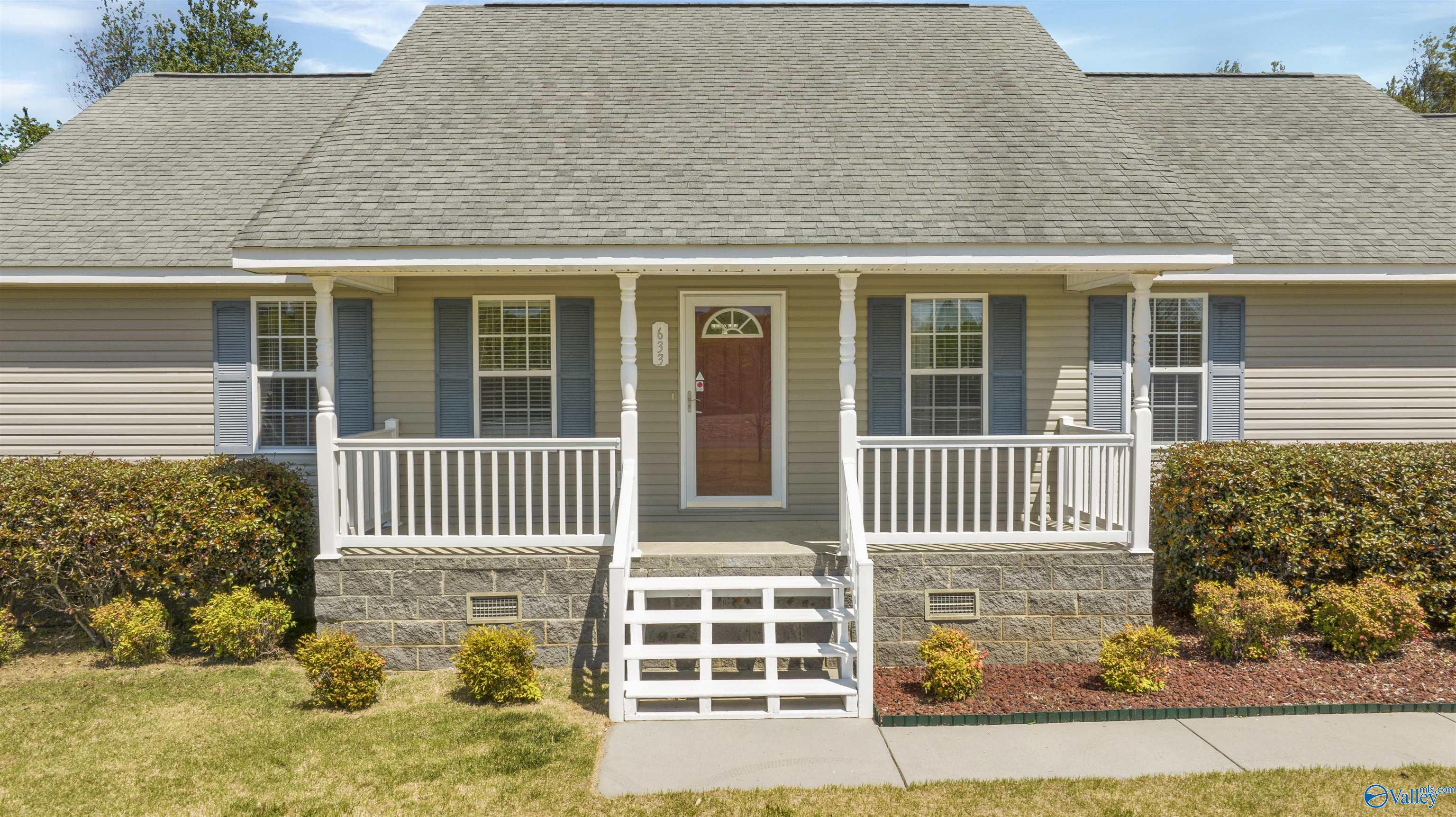 Home front with a covered porch, white railings, central steps, and a red front door.