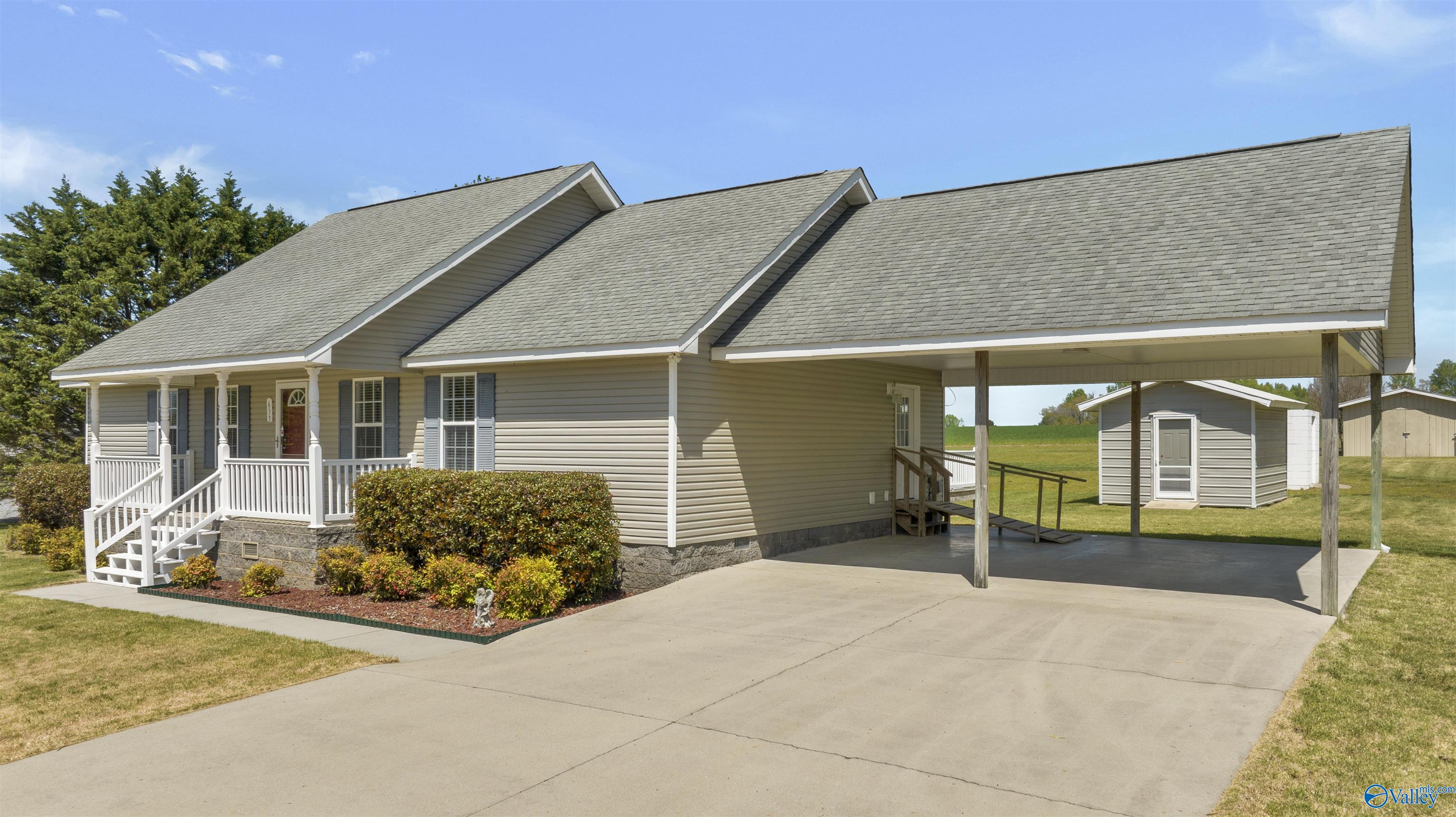Beige house with a white front porch, expansive covered carport, and detached shed.
