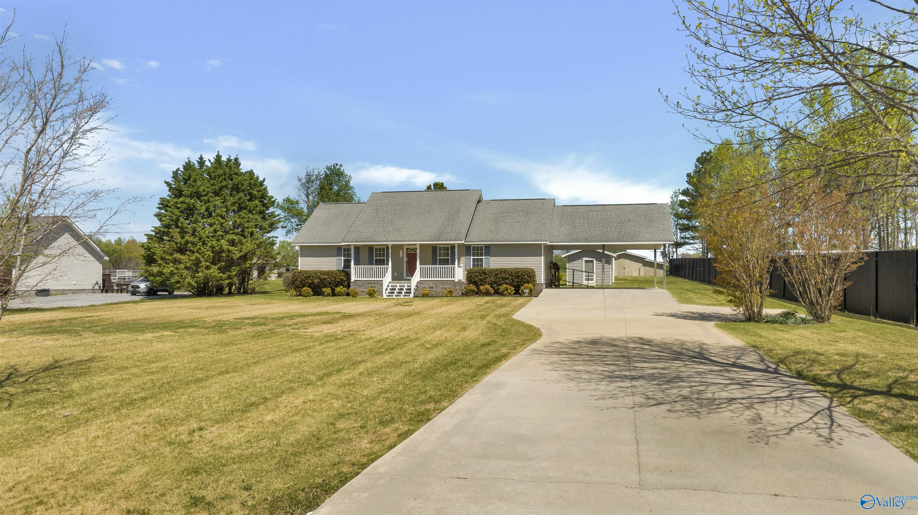 Gray single-story home with a covered porch, carport, and broad concrete driveway.