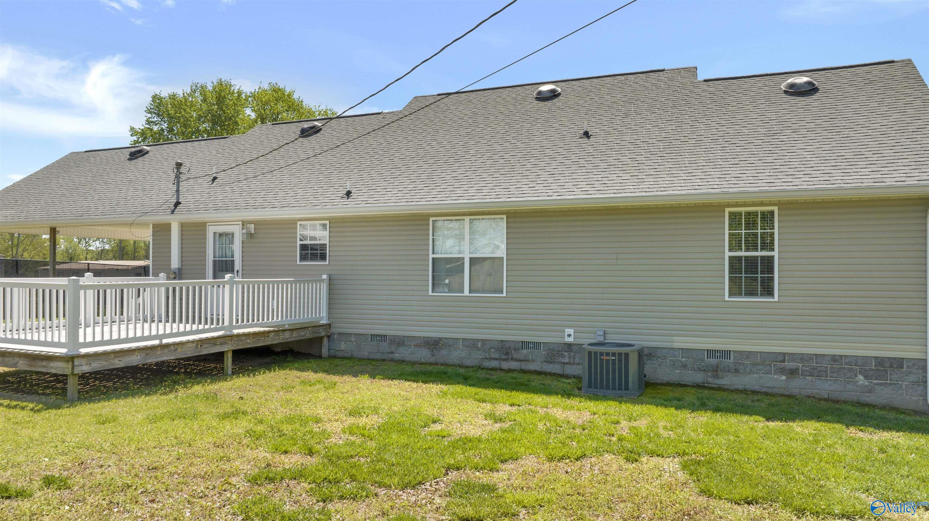 Rear of a gray-sided house with a white-railed deck and broad shingled roof.