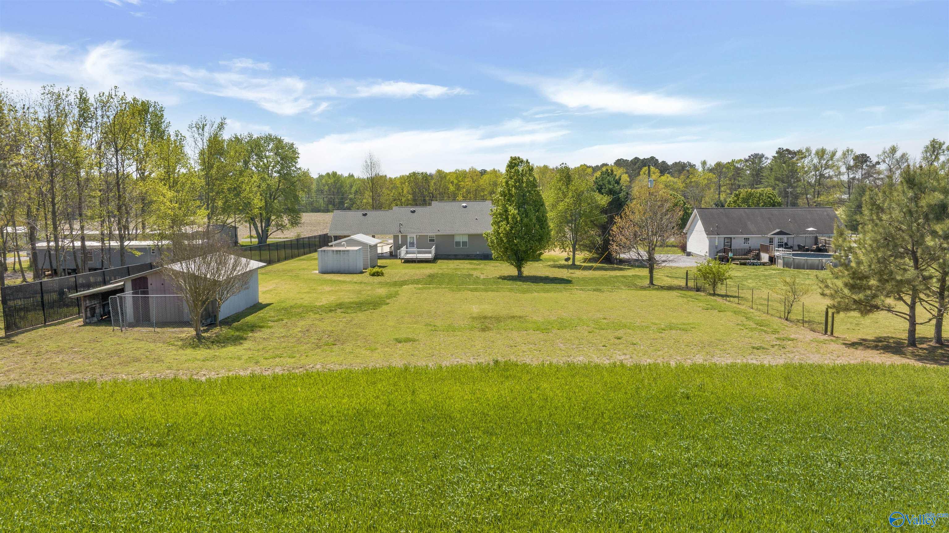 Aerial view of a home beyond a broad lawn, with a small outbuilding and fenced yard.