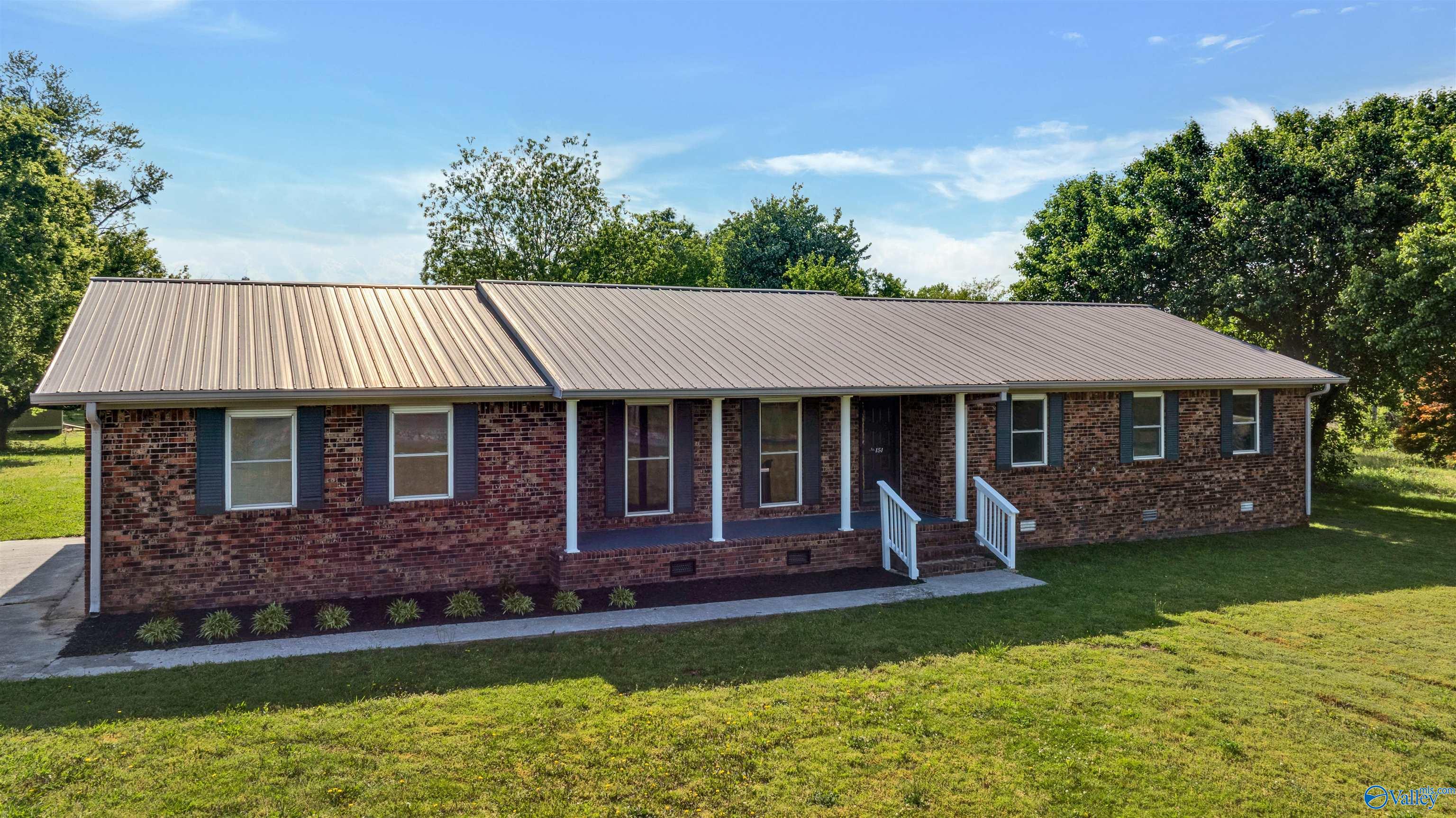 Single-story brick house with a long metal roof, covered porch, and white entry railings.