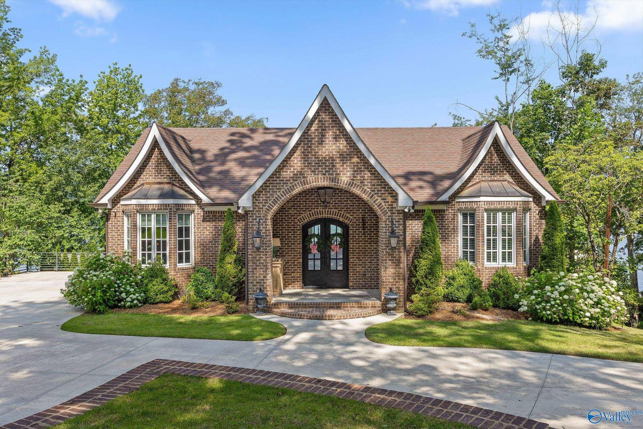 Brick house with white-trimmed gables, arched entry, landscaped yard, and curved driveway.