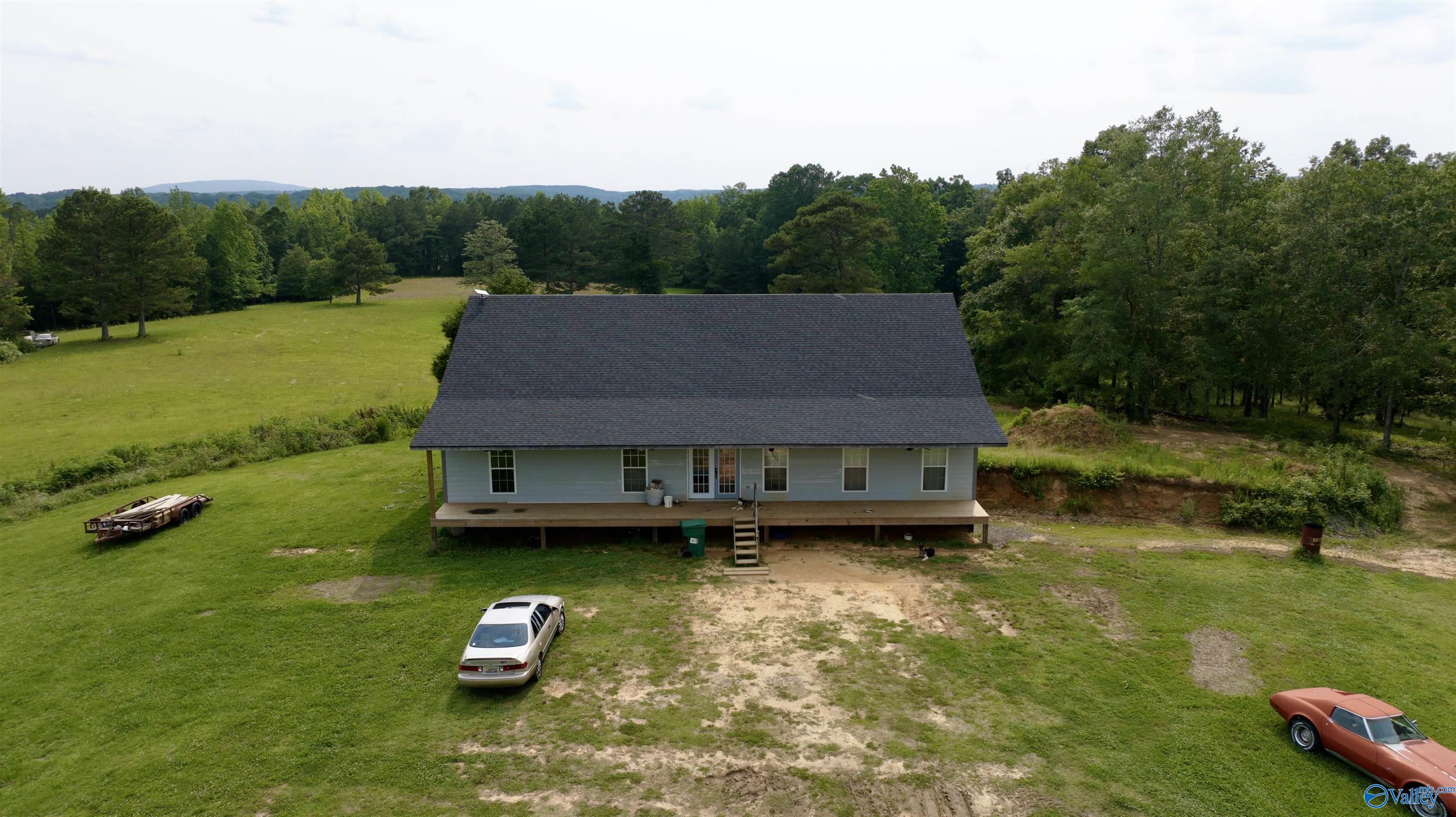 Aerial view of a single-story house with a long porch, spacious grassy yard, and wooded surroundings.