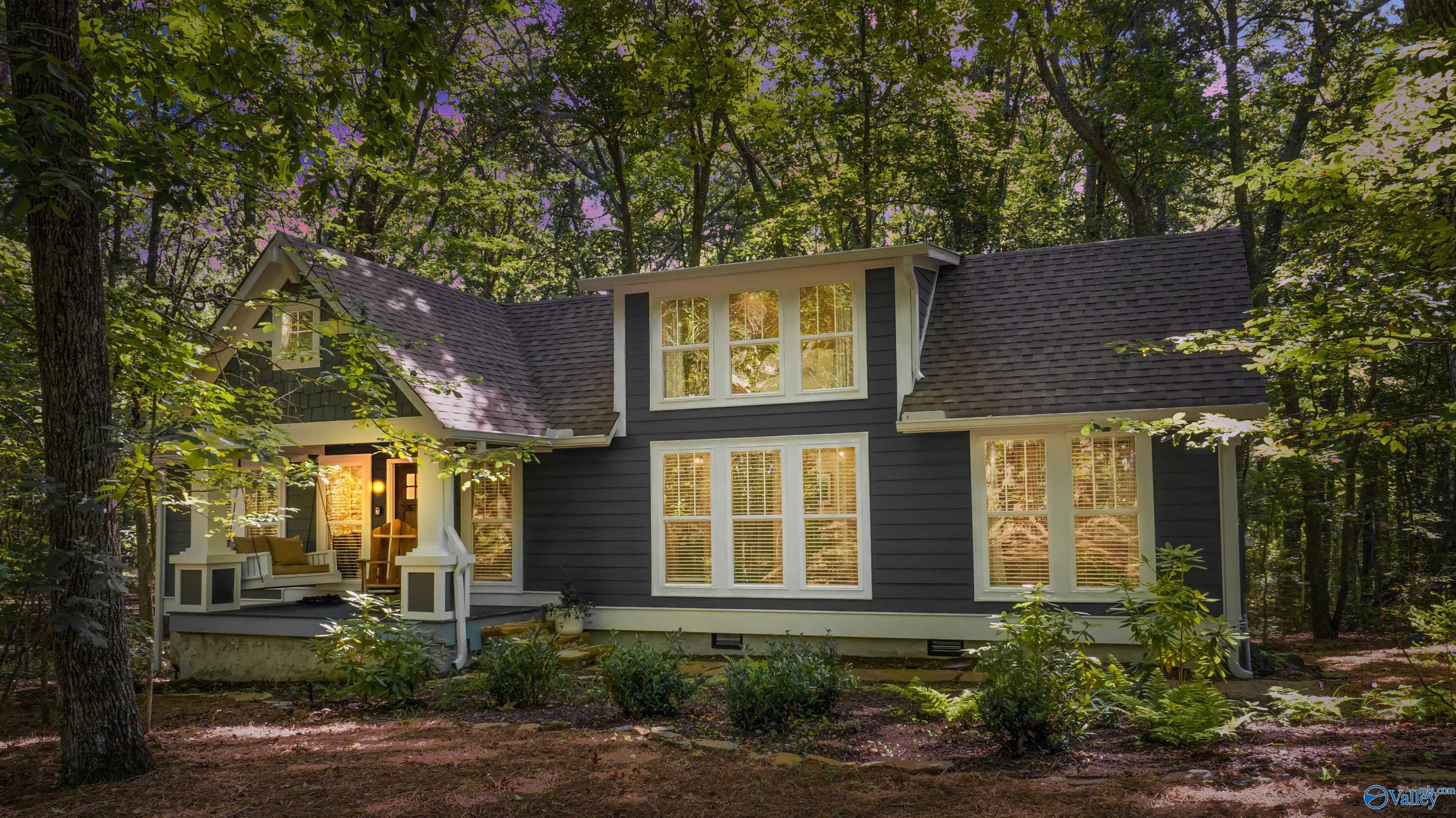 Dark gray two-story house with a furnished porch nestled among mature trees.