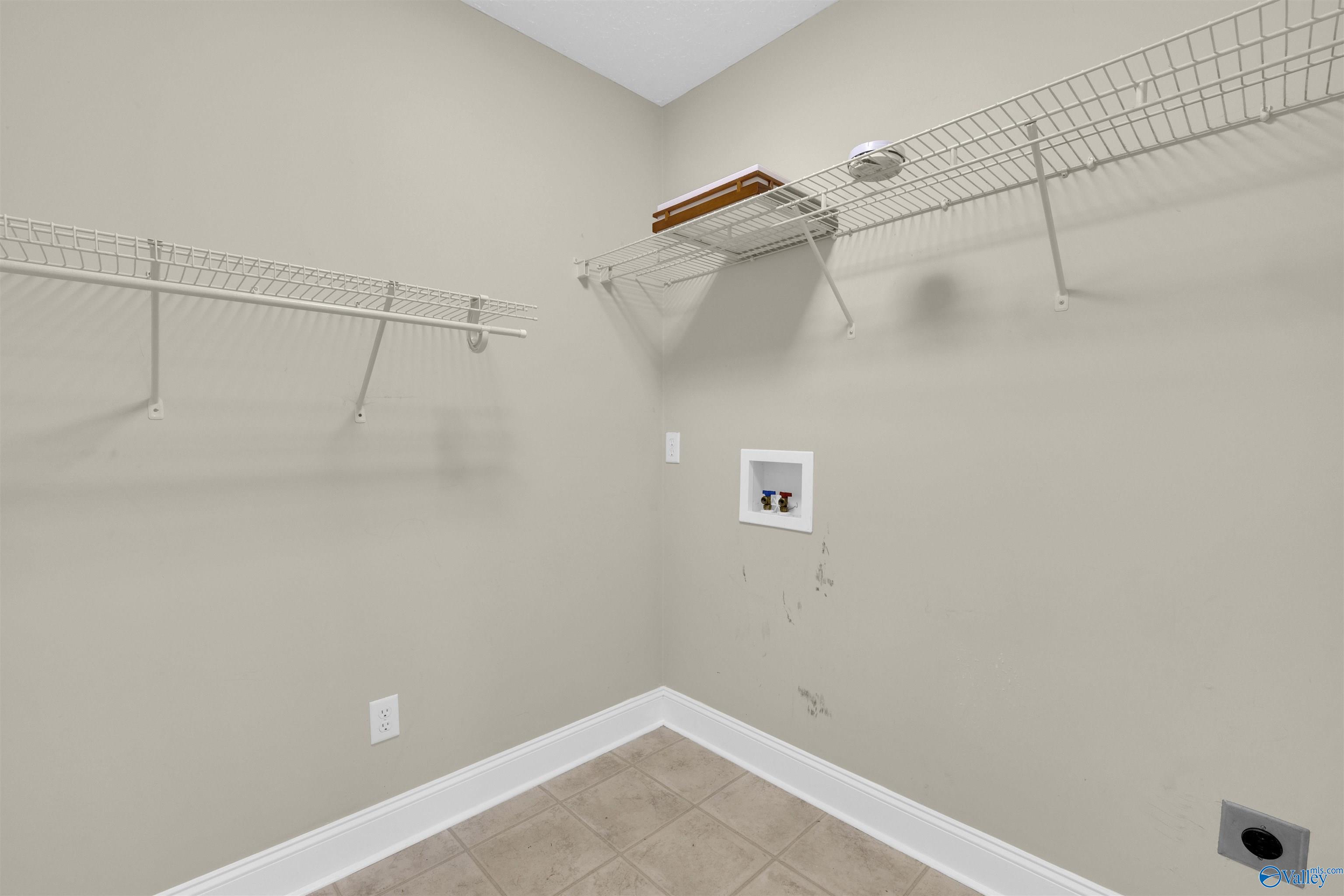 Empty laundry room with wire shelving, washer hookups, and scuff marks on beige walls.
