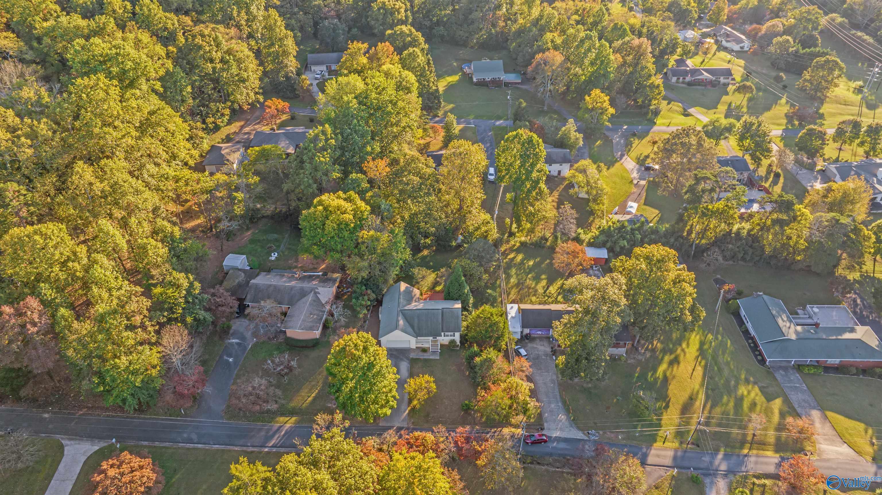 Aerial view of a home among mature trees and neighboring houses in autumn.