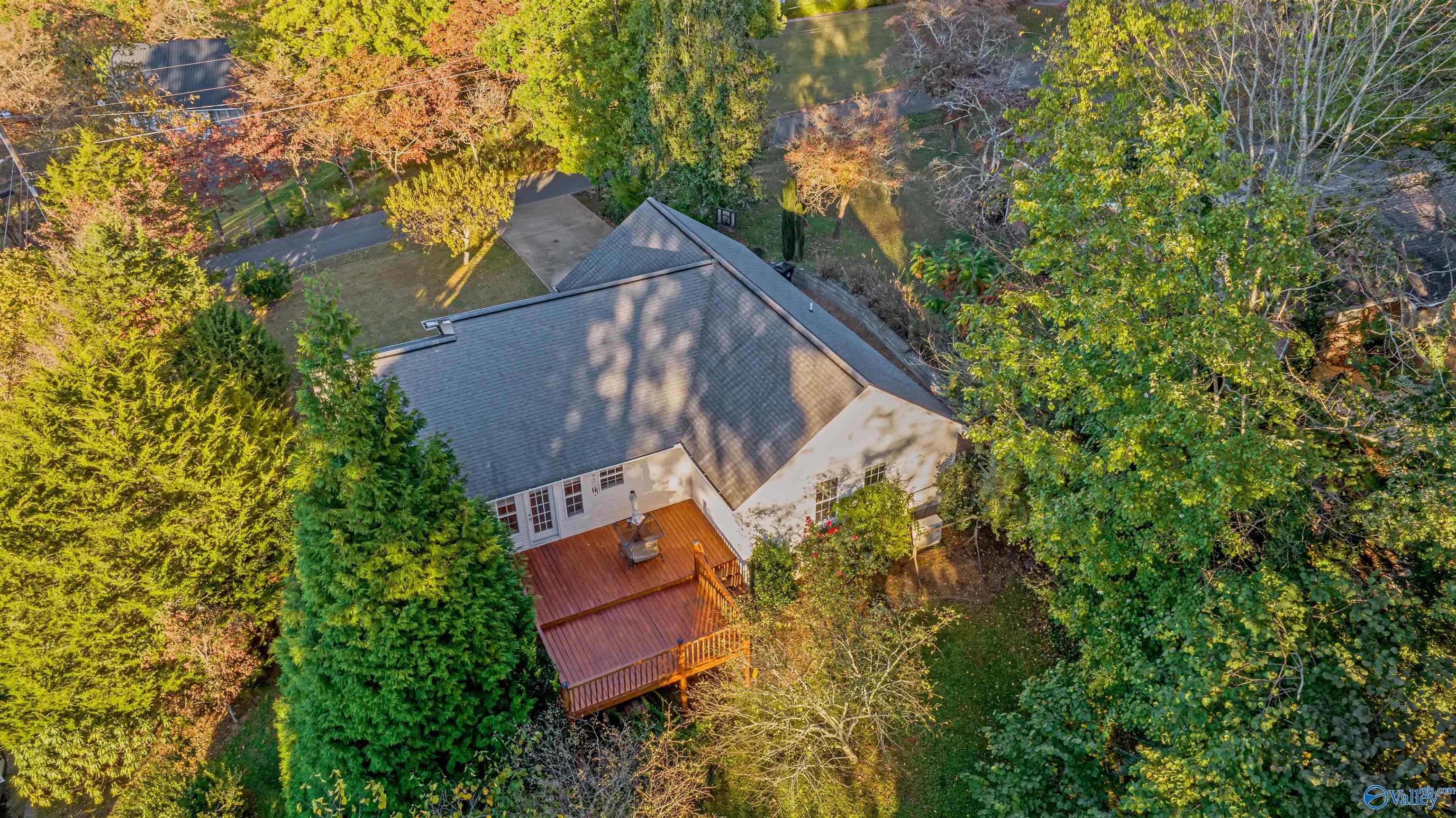 Aerial view of a tree-surrounded home with a large raised backyard deck.