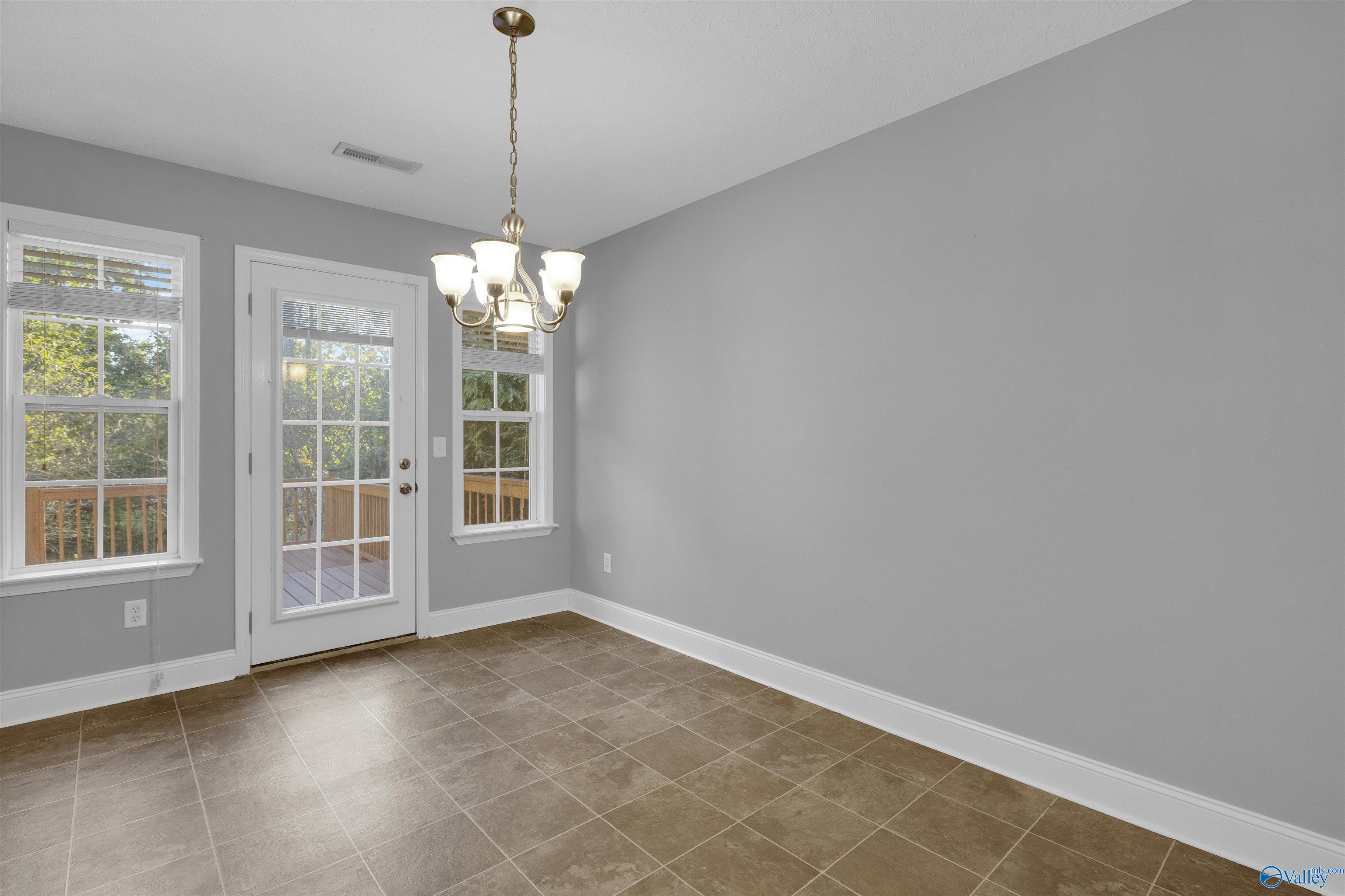 Empty dining area with brown tile floors, a brass chandelier, and a glass door opening onto a deck.