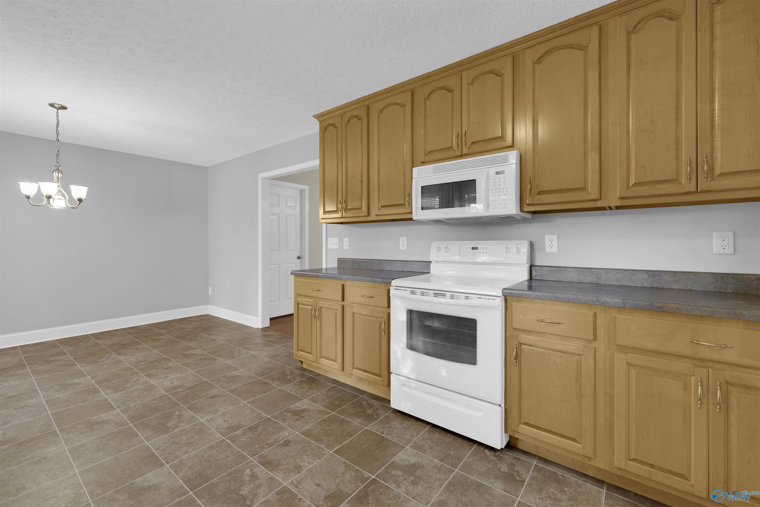 Kitchen with honey-colored cabinets, gray countertops, white appliances, and brown tile flooring.