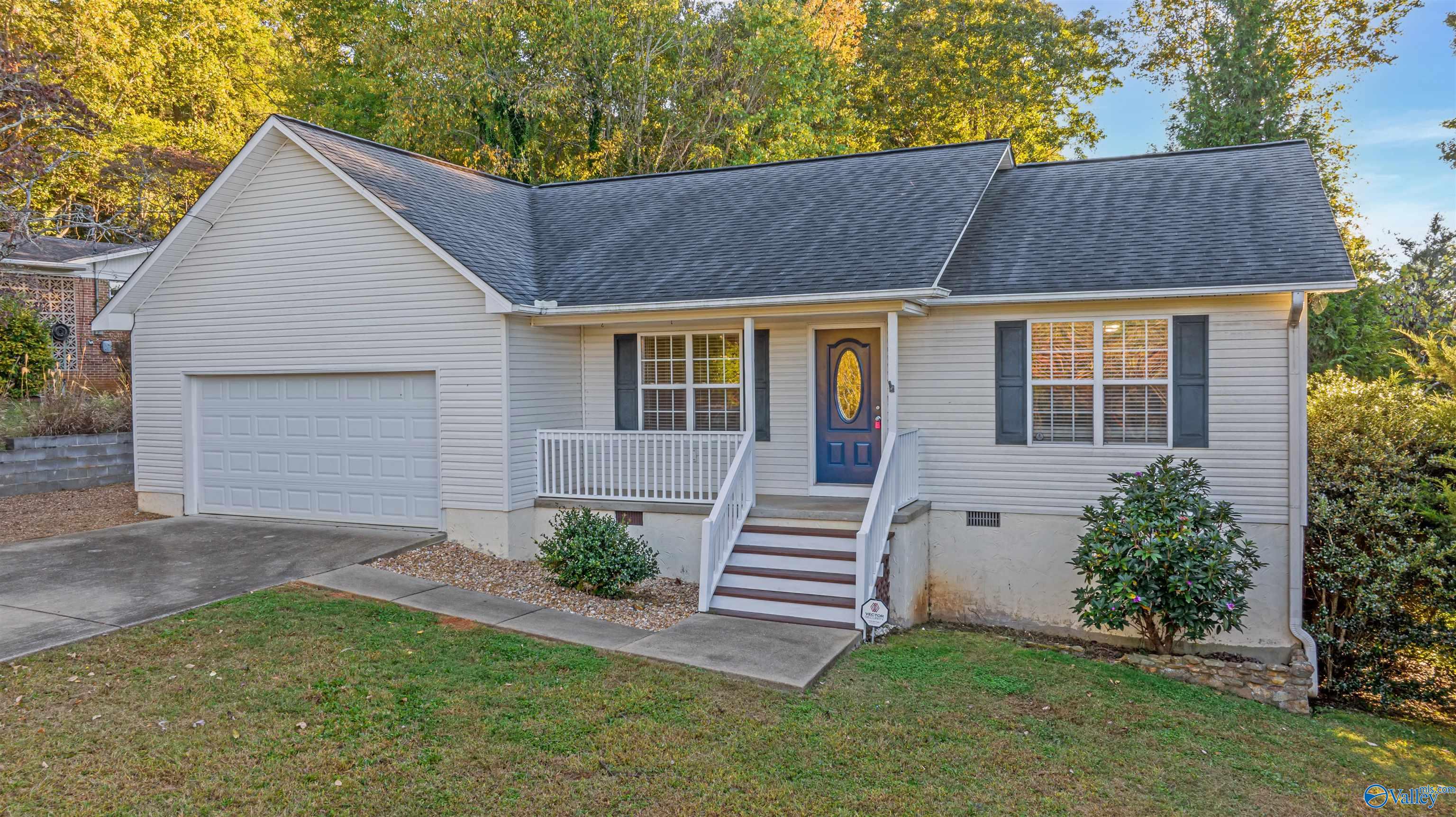 Single-story home with an attached garage and raised front porch surrounded by autumn trees.