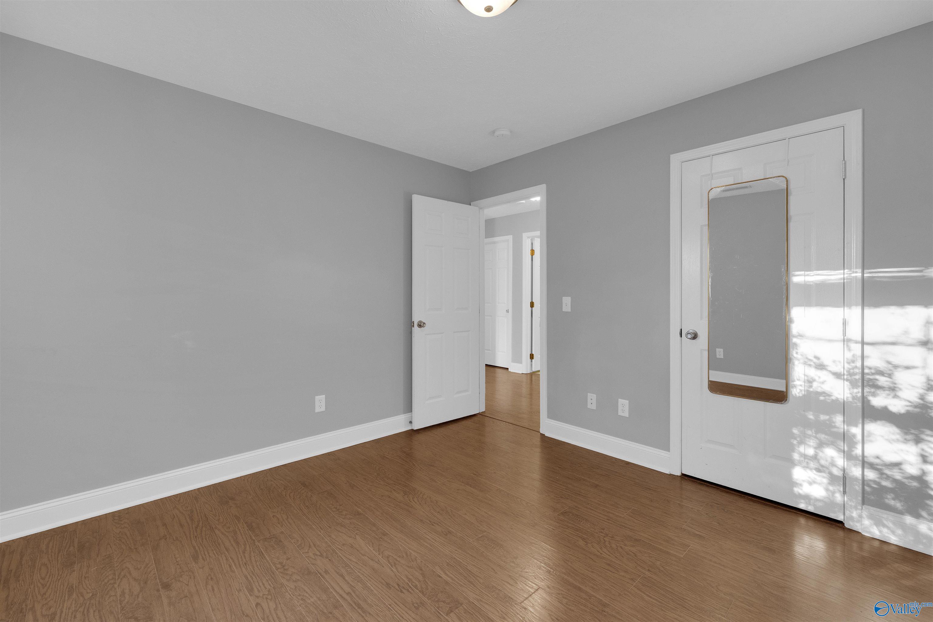 Vacant bedroom with gray walls, wood flooring, and a narrow mirror on the closet door.