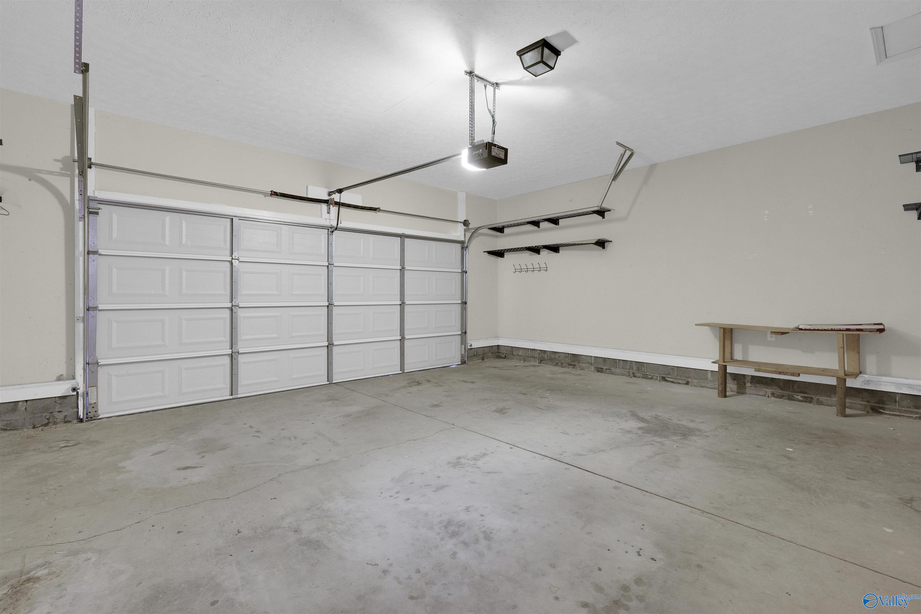 Empty garage with a wide overhead door, wall shelves, and a workbench.