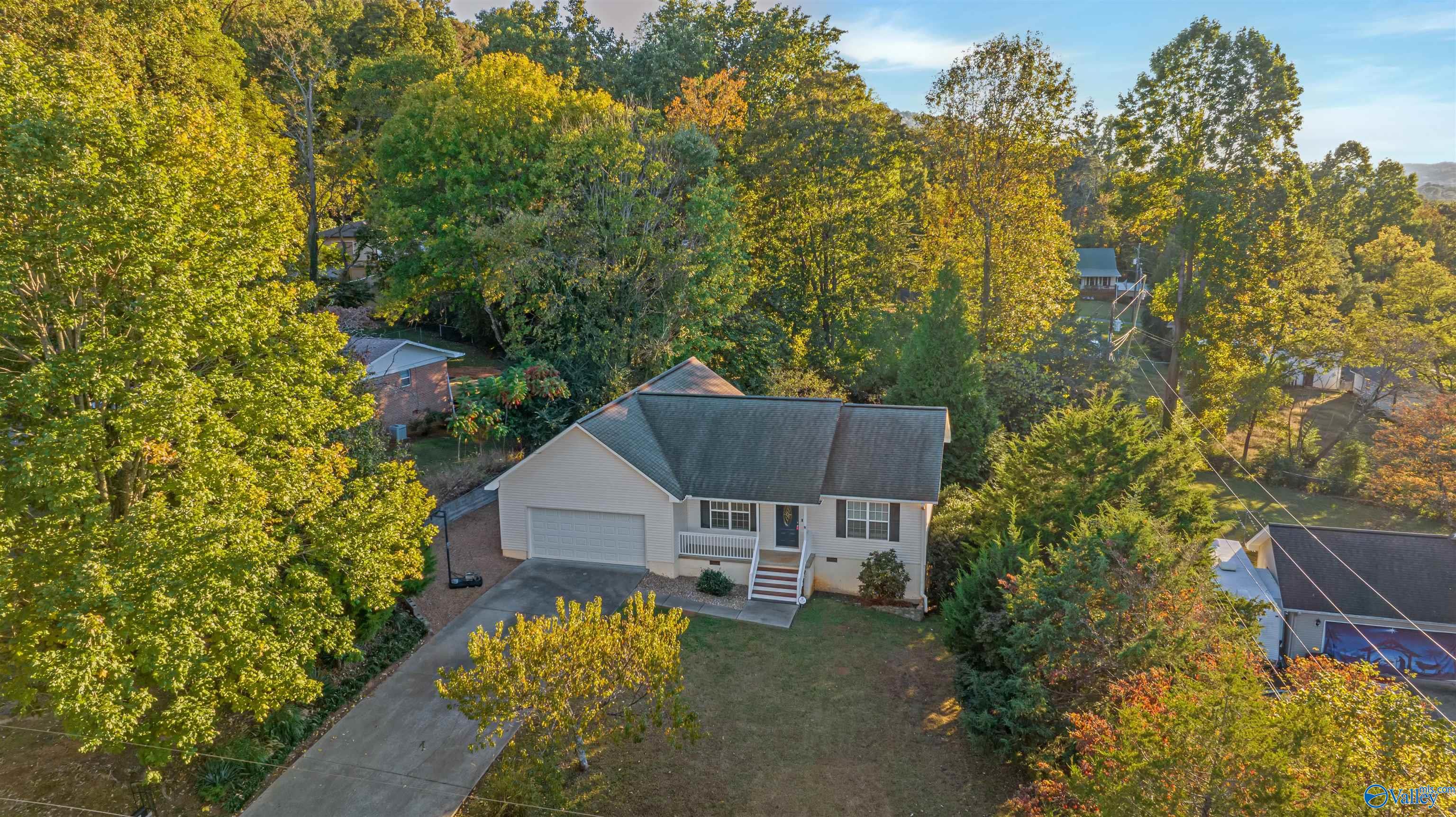 Aerial view of a single-story home with an attached garage, driveway, and autumn trees.