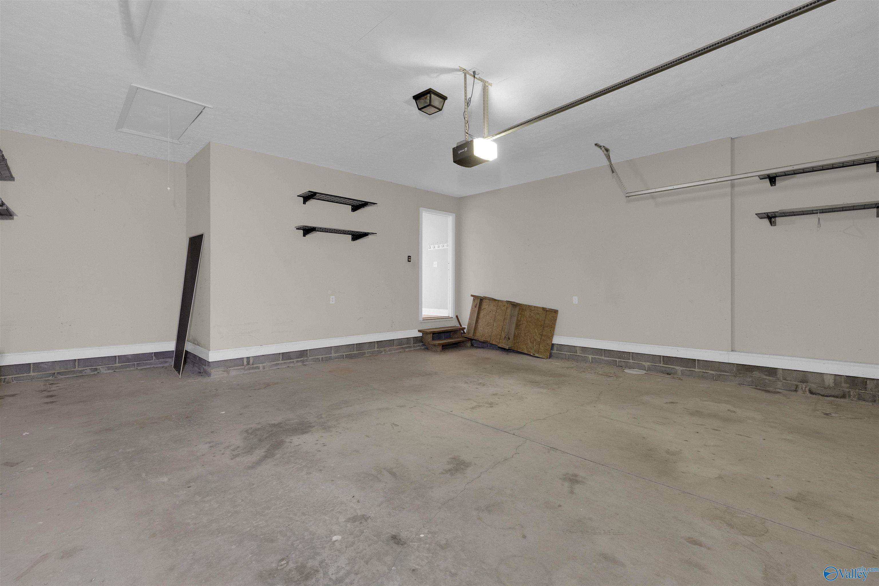 Empty garage with concrete floor, wall-mounted shelves, and a door to the house.