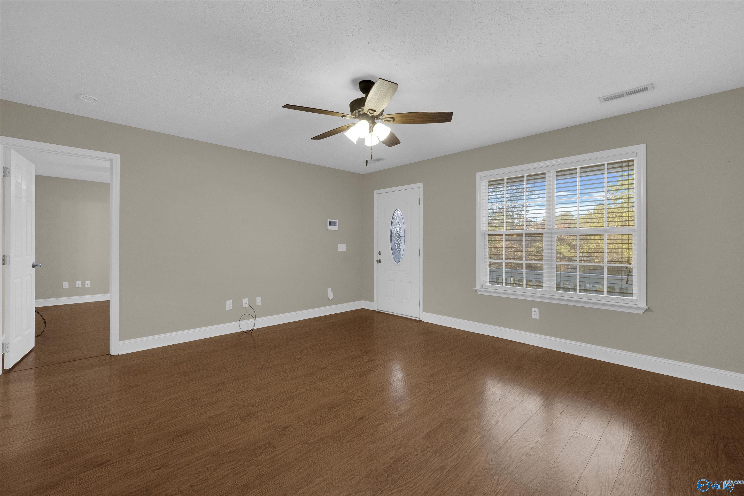 Empty room with wood flooring, a ceiling fan, and a large window with white blinds.