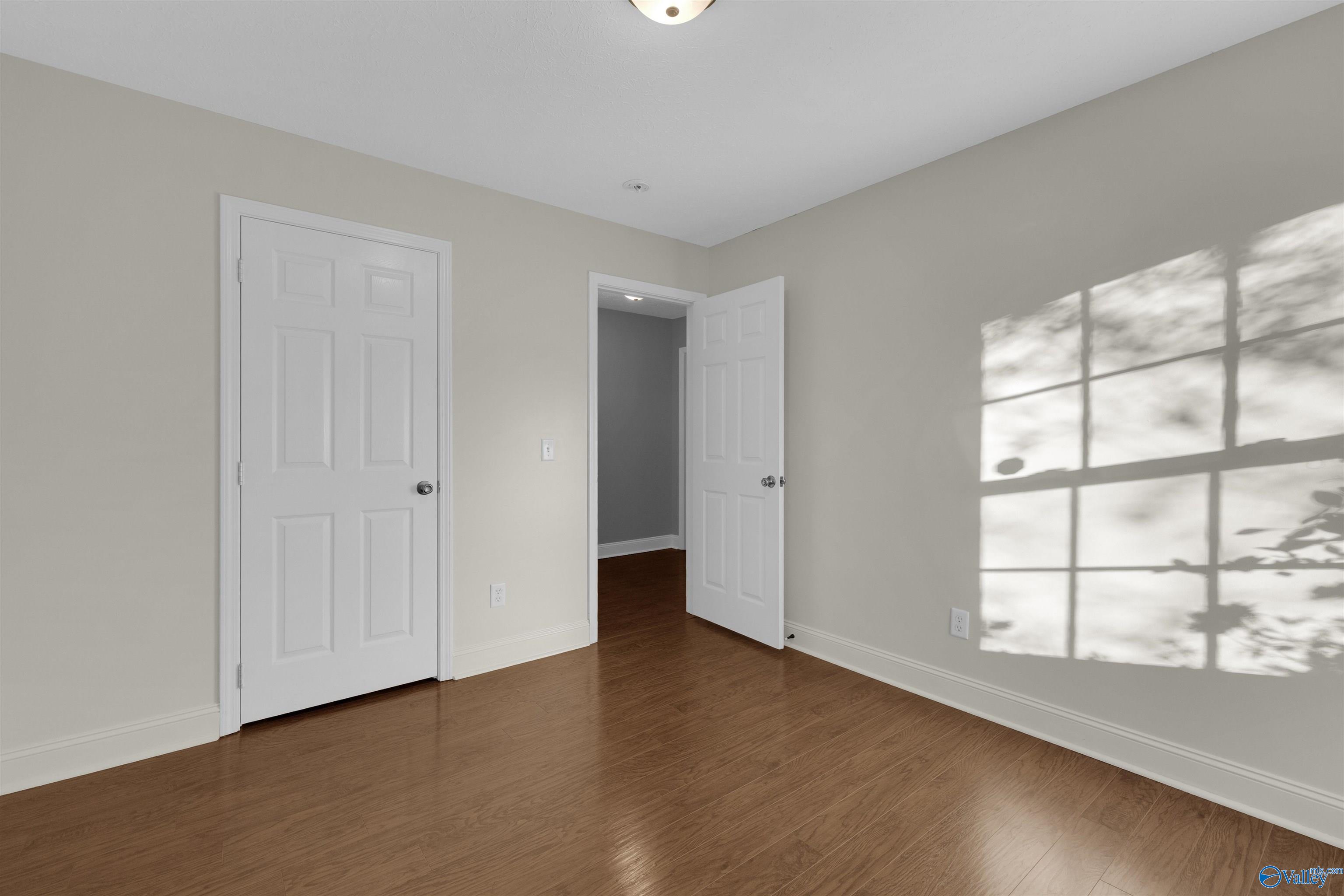 Empty room with hardwood floors, white paneled doors, and sunlight casting a window-grid shadow.