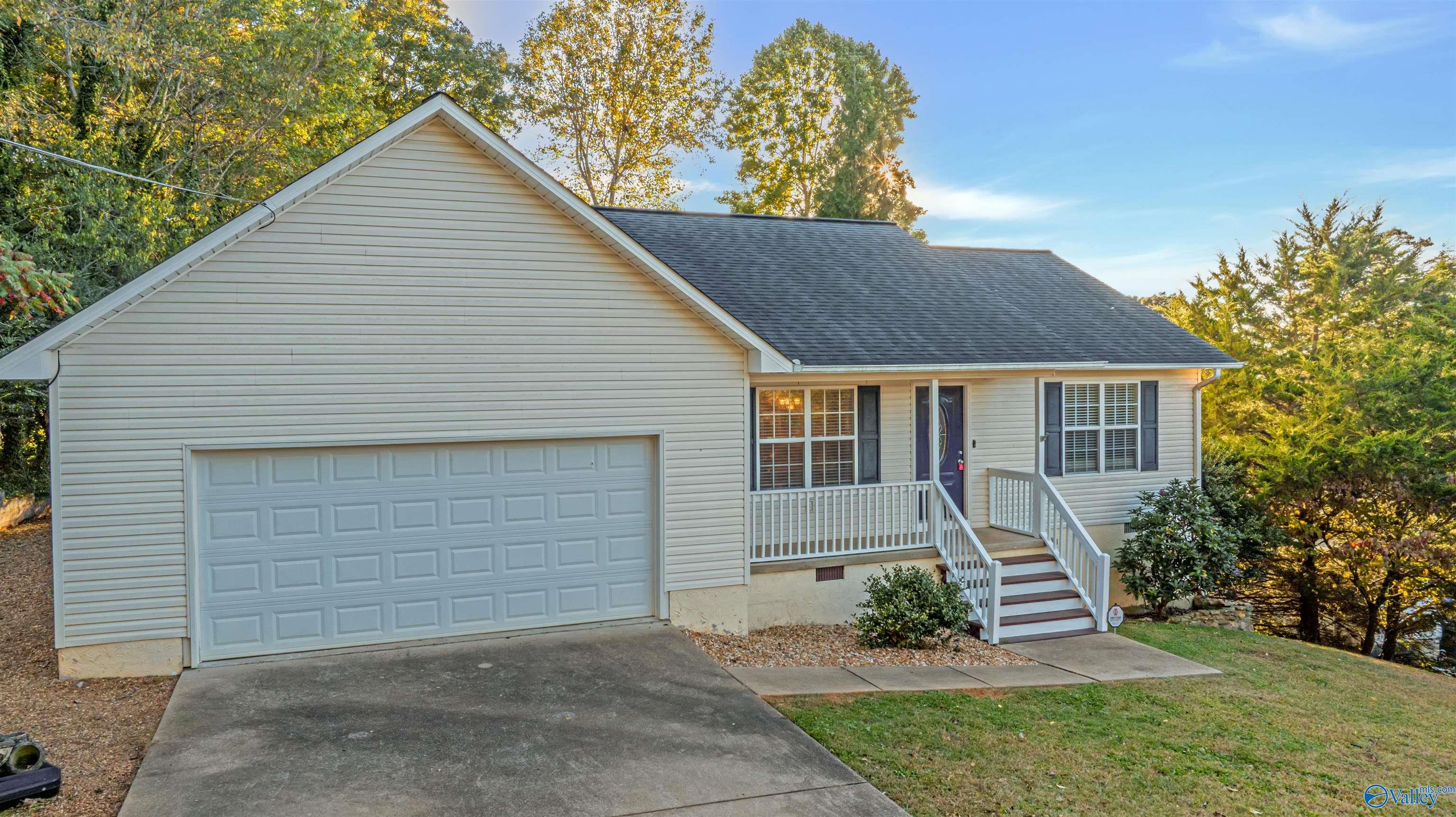 Light-sided home with a two-car garage and front porch among mature autumn trees.