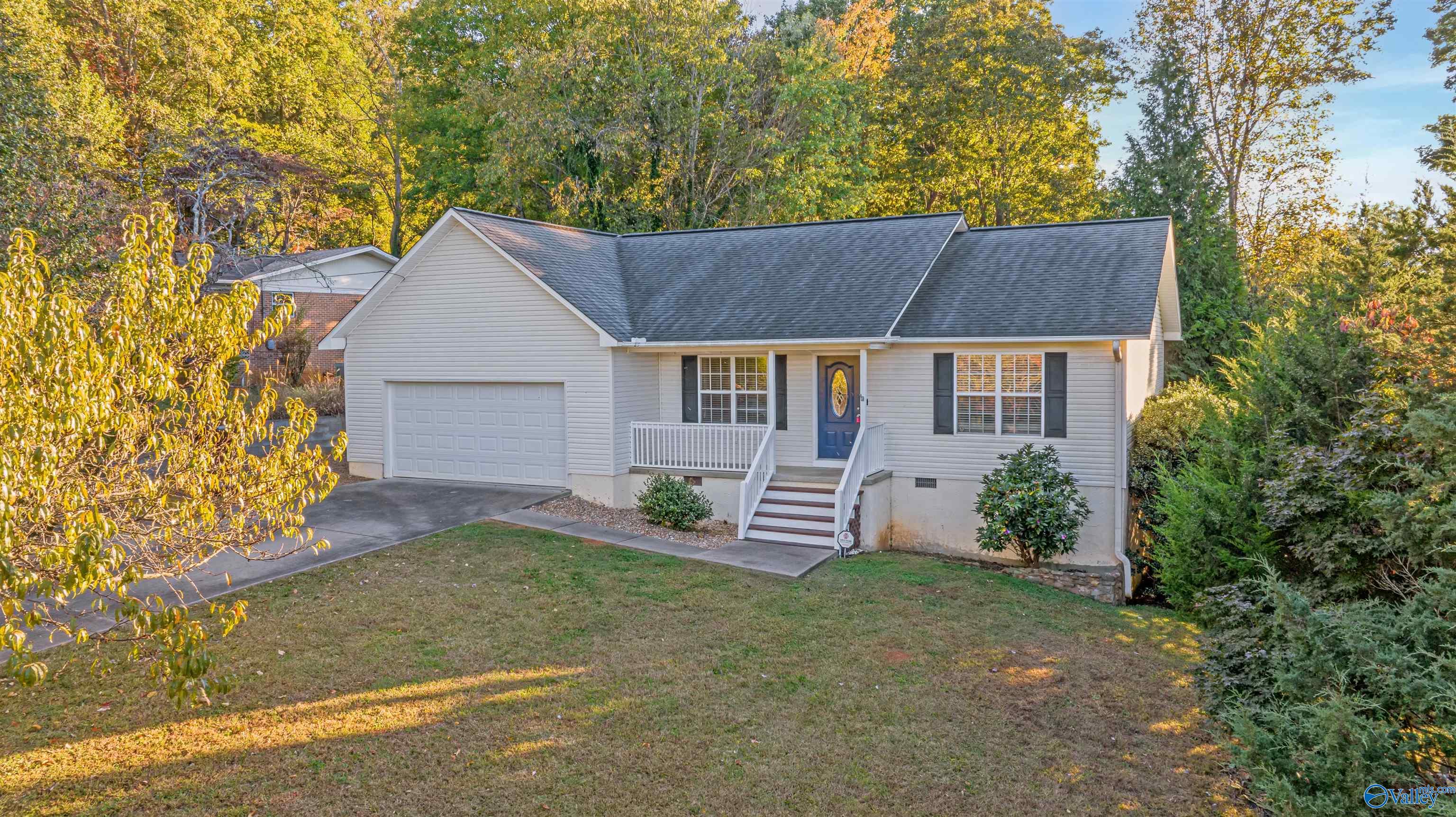 Light-gray single-story home with an attached garage, blue front door, and wooded autumn setting.
