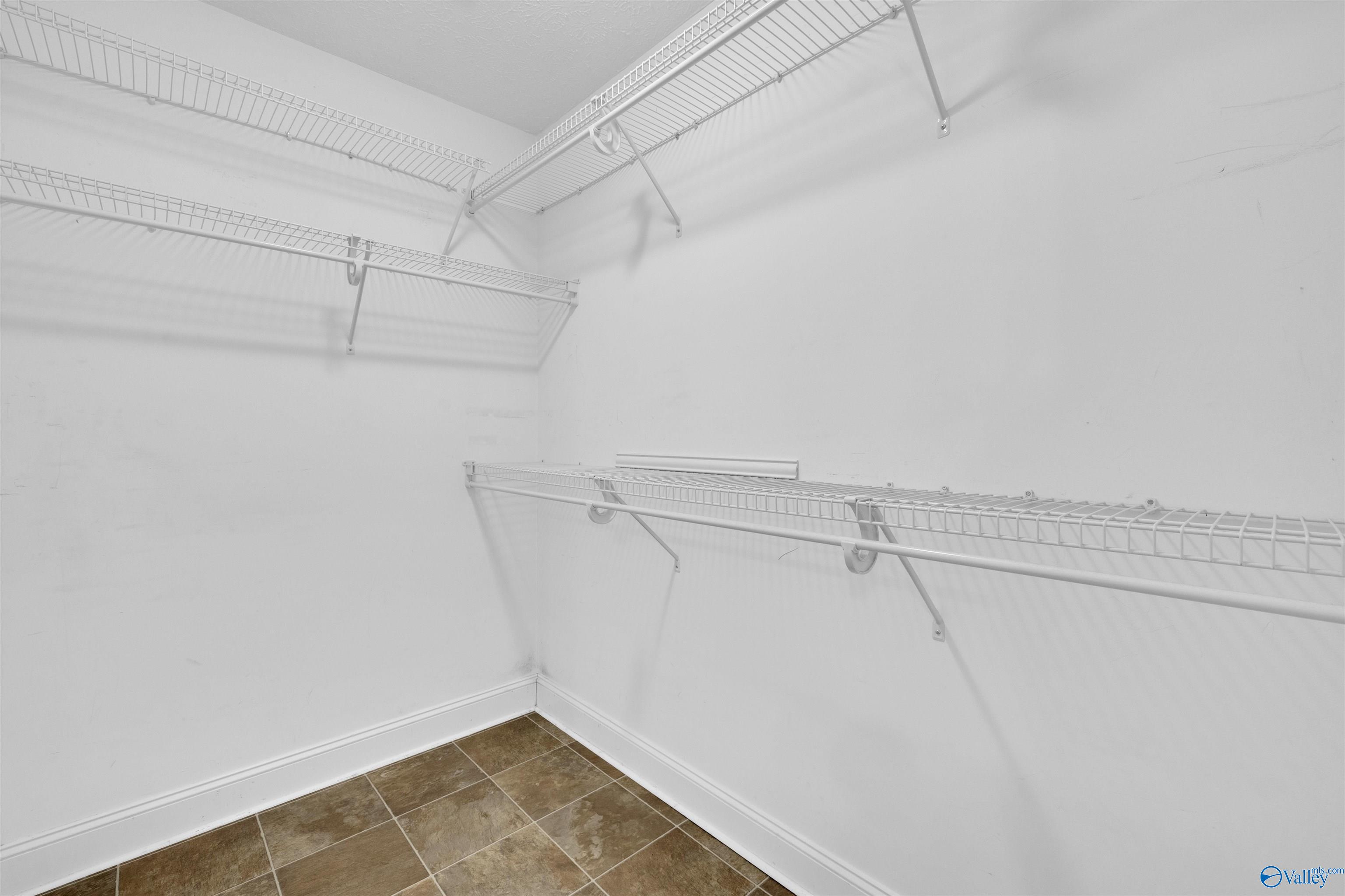 Empty walk-in closet with extensive white wire shelving and a brown tiled floor.