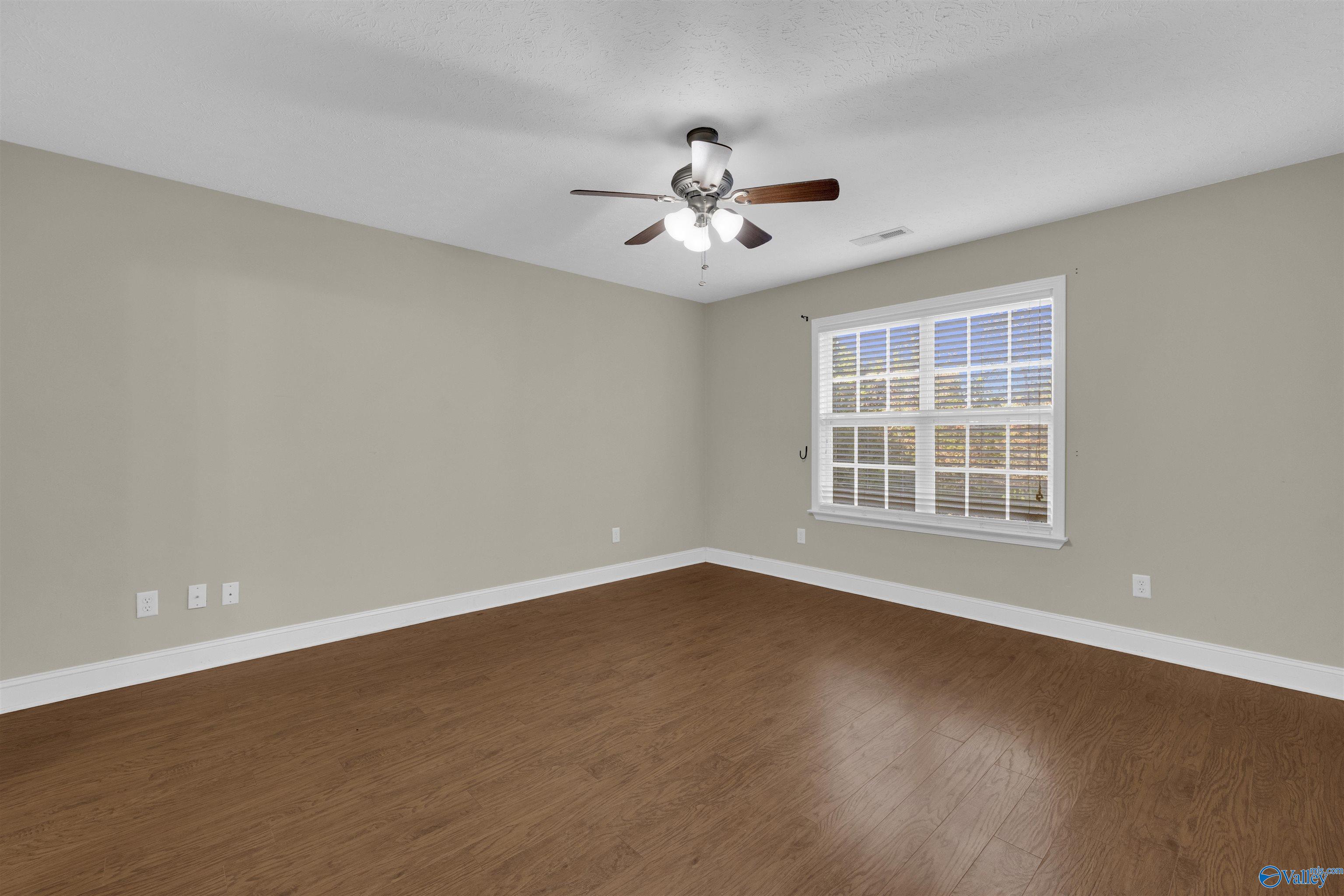 Empty room with wood-look floors, beige walls, a large window with blinds, and a ceiling fan.