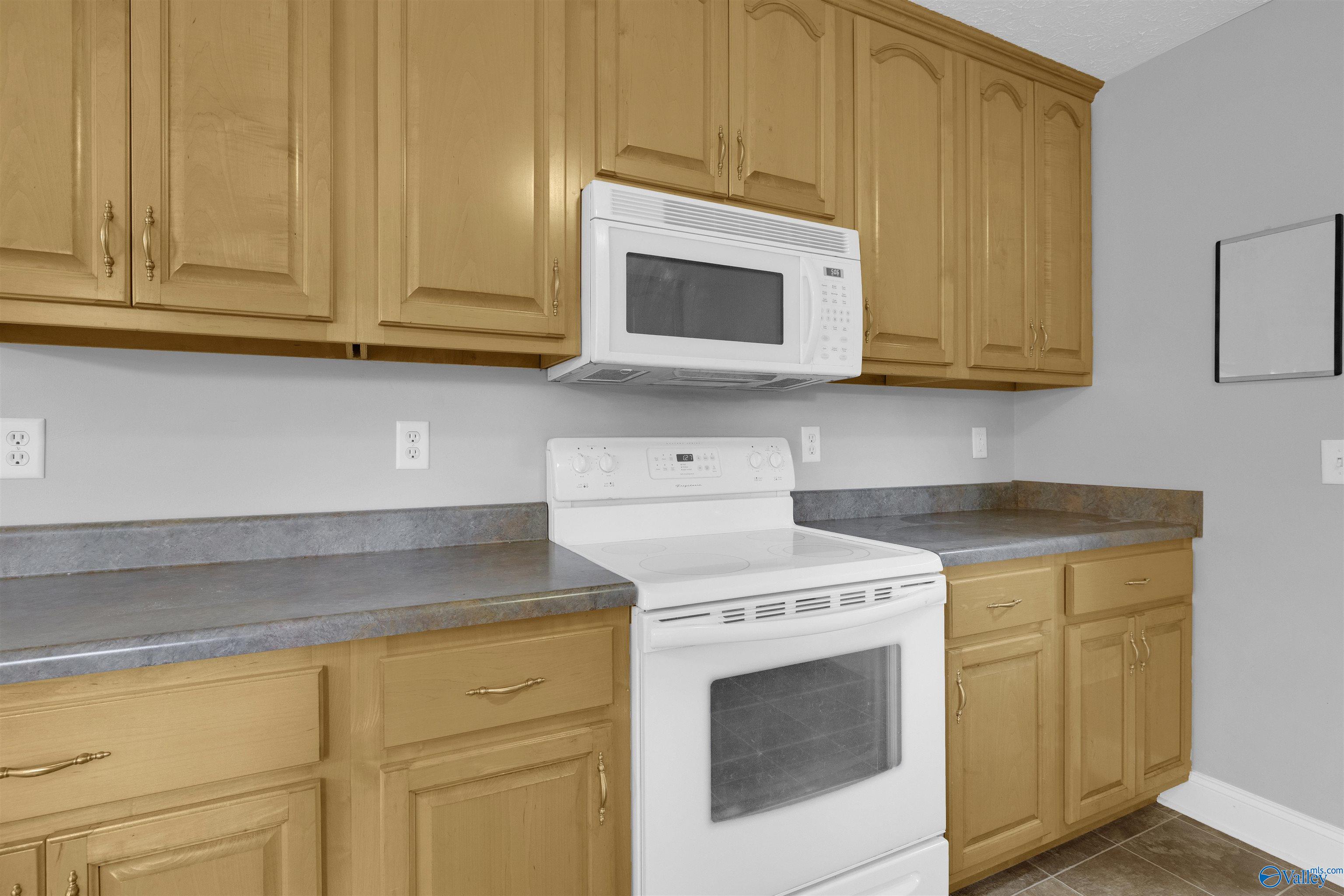 Kitchen with honey-colored cabinets, gray countertops, and a white range and microwave.