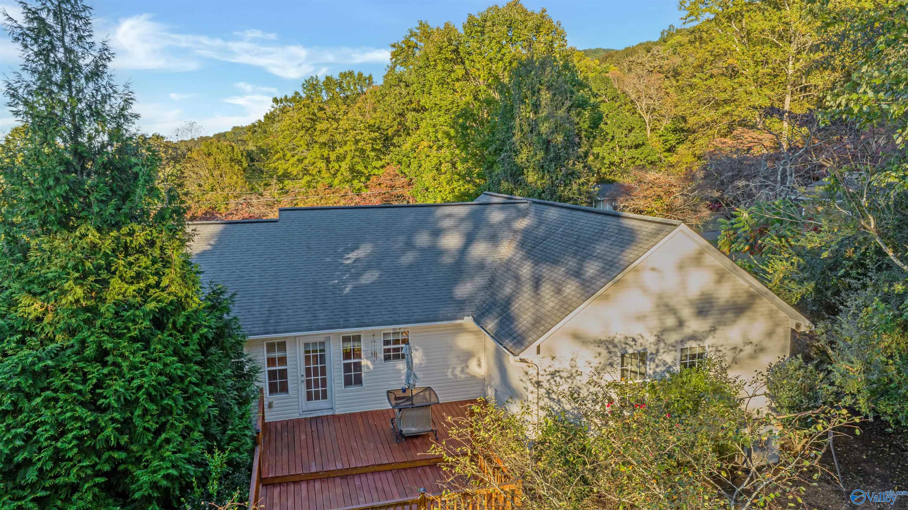 Rear of a light-colored house with a large multi-level deck, surrounded by dense autumn trees.