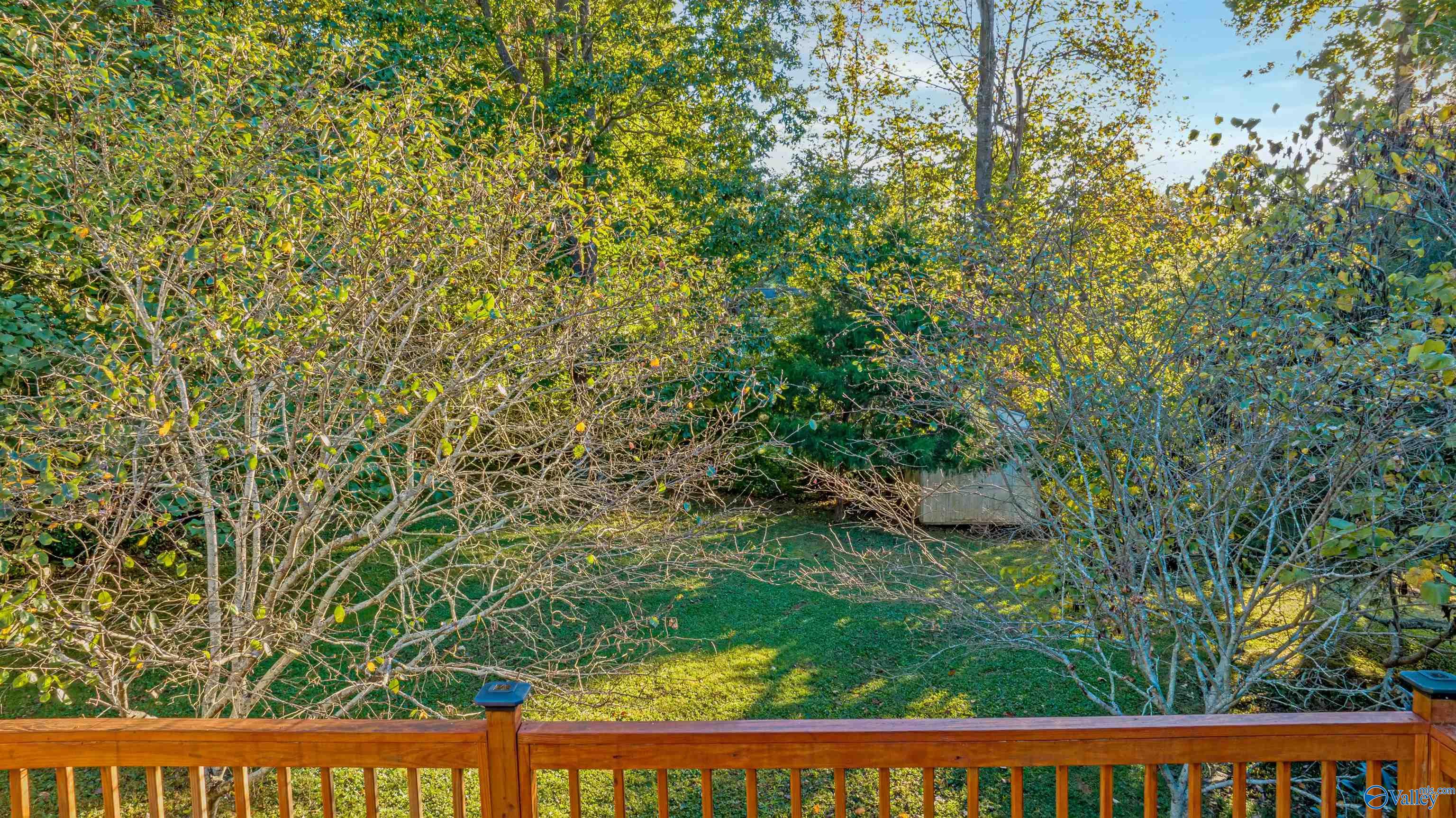 Wooden deck overlooks a leafy backyard with a grassy lawn and a small waterway.