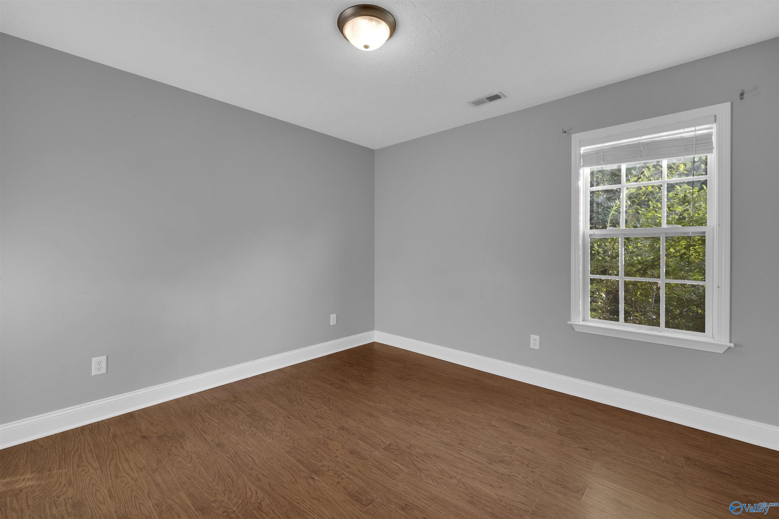Empty room with wood flooring, gray walls, and a large window overlooking greenery.