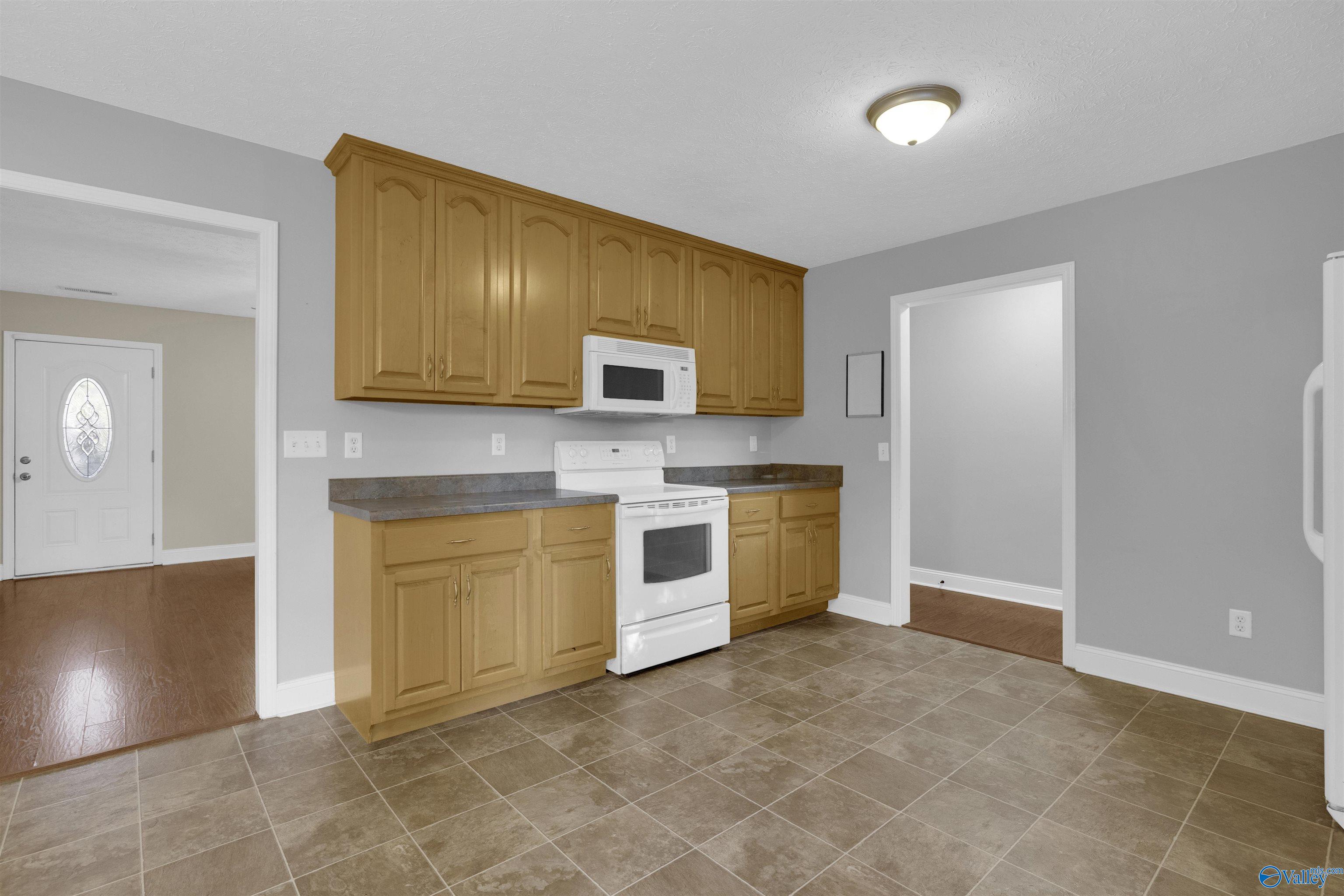 Kitchen with honey-colored cabinets, brown tile flooring, and white range and microwave.