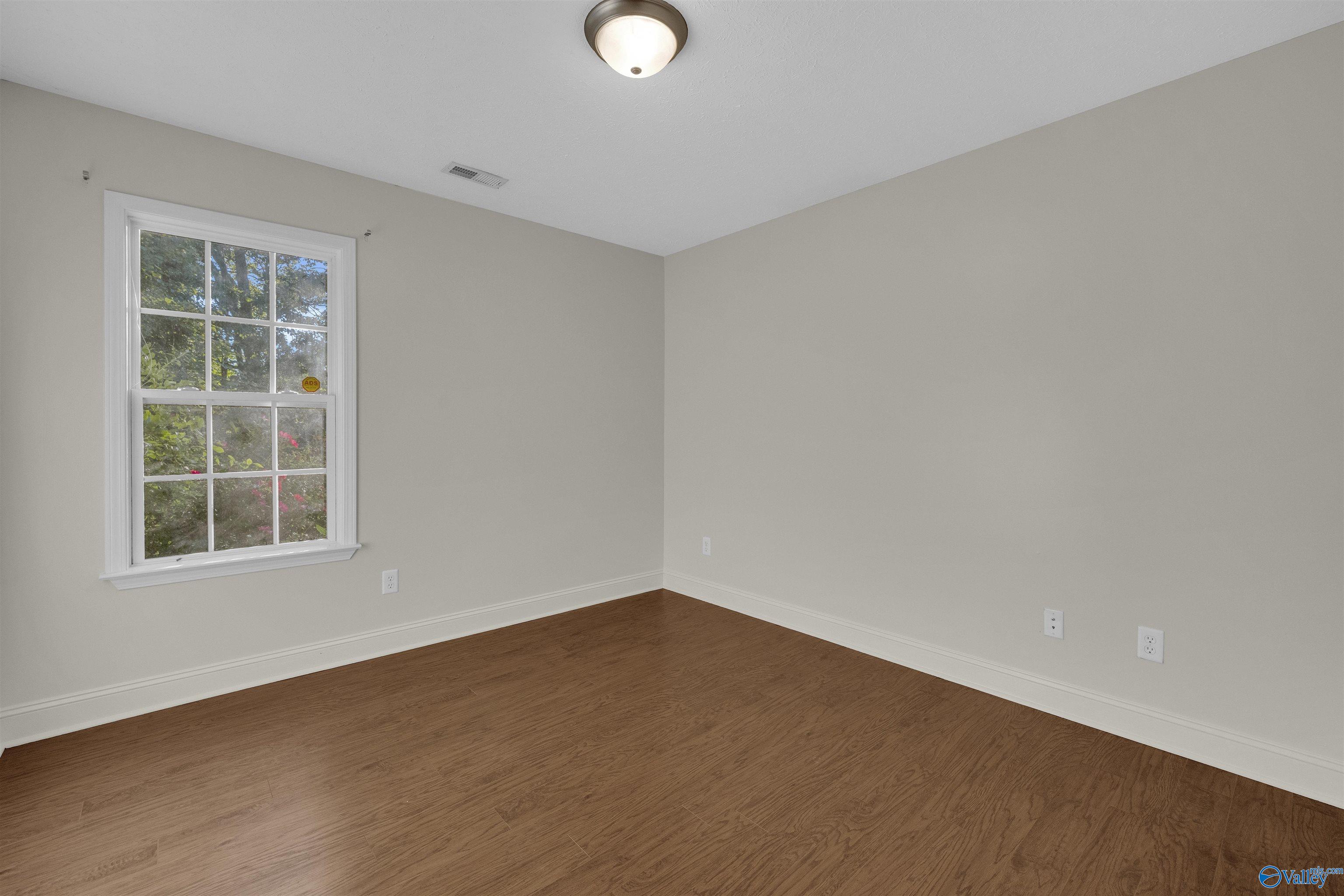 Empty room with brown wood-look flooring and a divided-pane window.