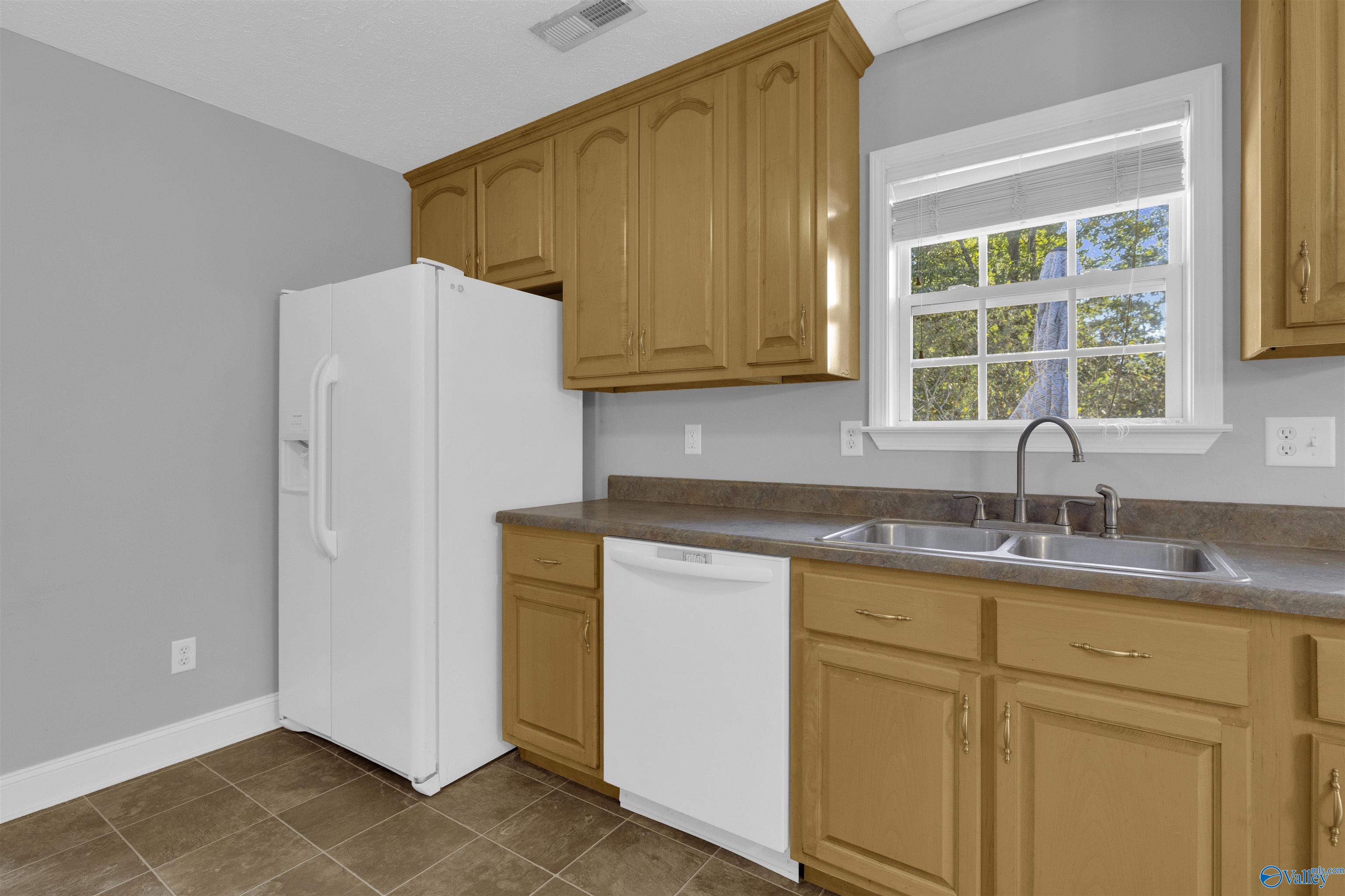 Kitchen with honey-colored cabinets, white appliances, and a double-basin sink beneath a window.