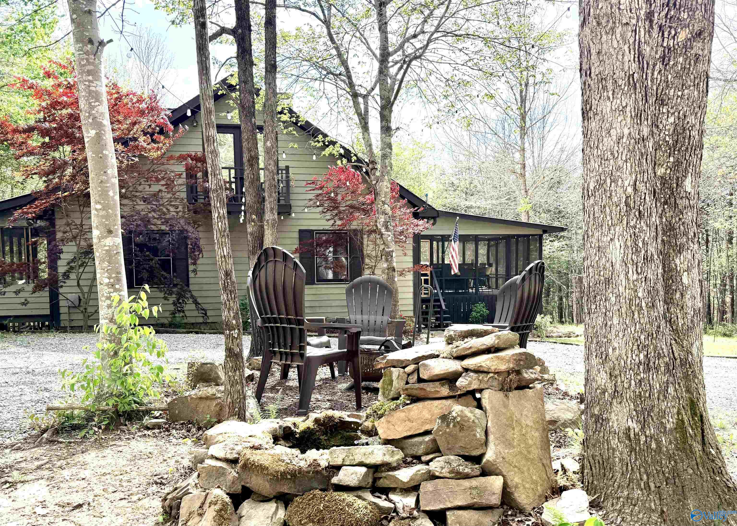 Wooded home with a screened porch and Adirondack chairs around a stone fire pit.