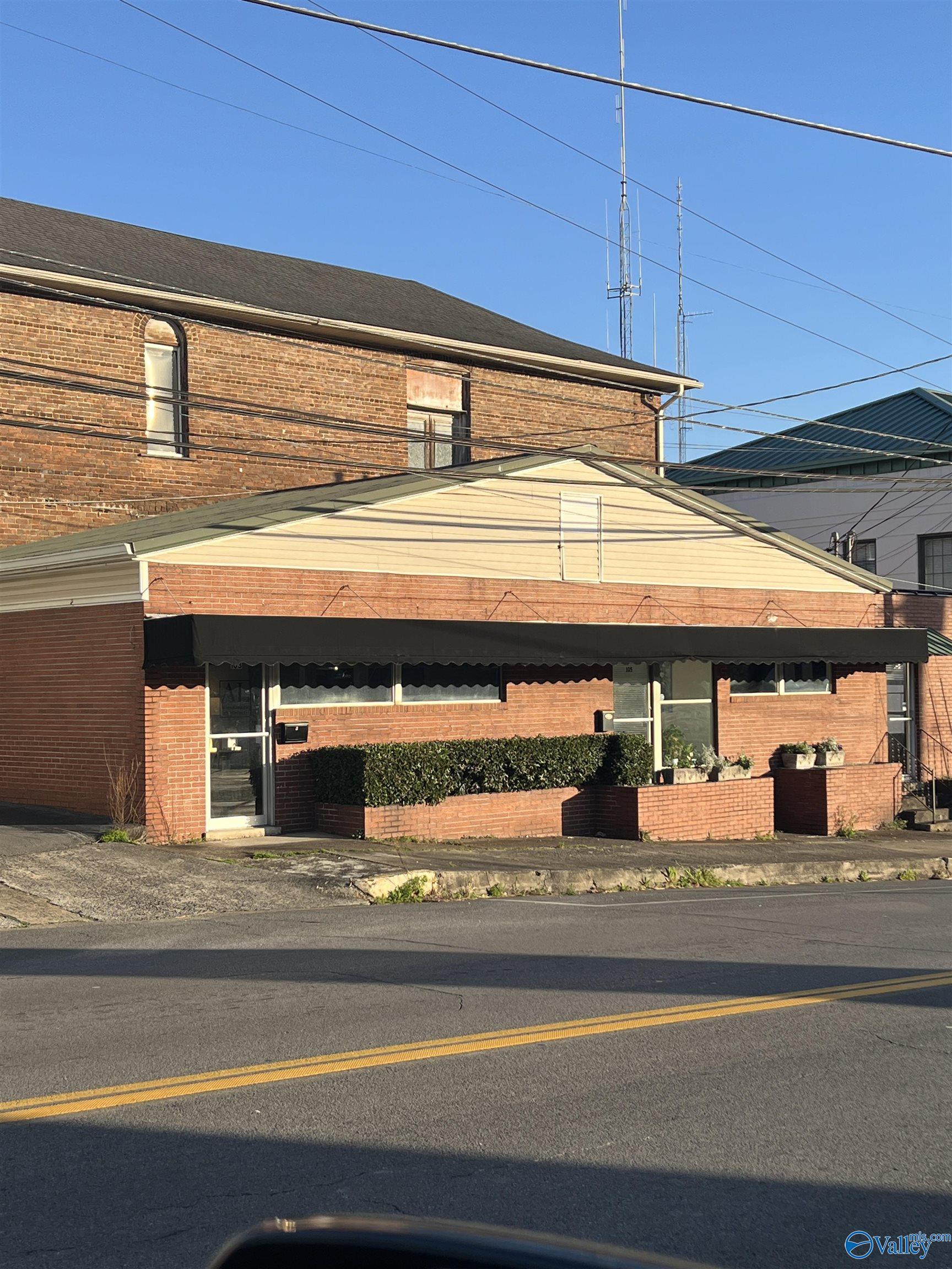 Red-brick commercial building with a cream gabled facade, dark awning, and brick planters.
