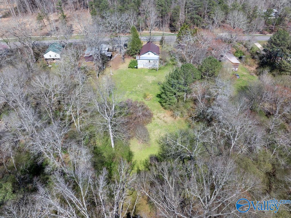 Aerial view of a red-roofed house with a grassy yard surrounded by trees.